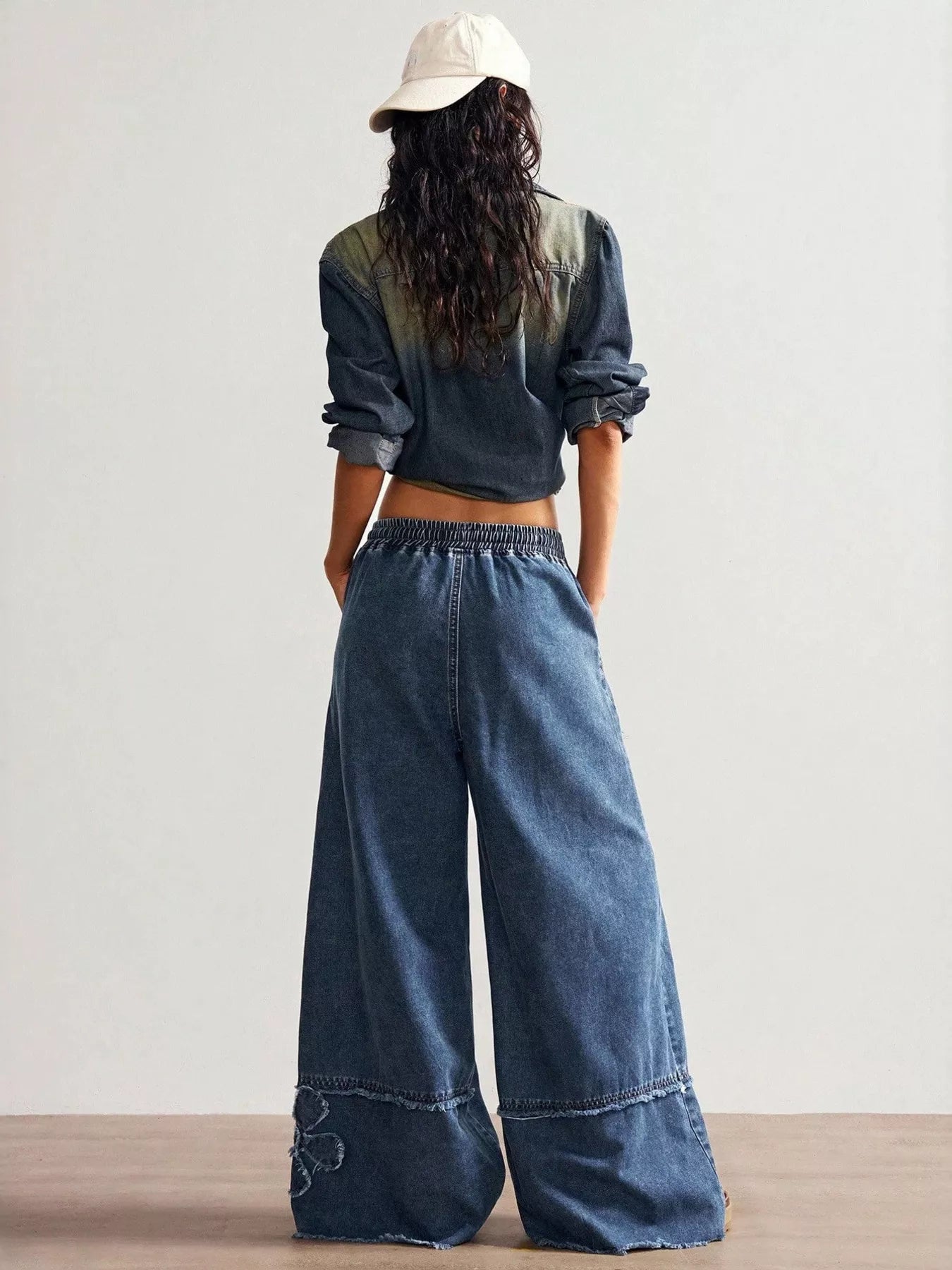 Wide-leg denim pants with drawstring waist, pockets, raw hem details, seam accents, and distressed floral appliqué designs.