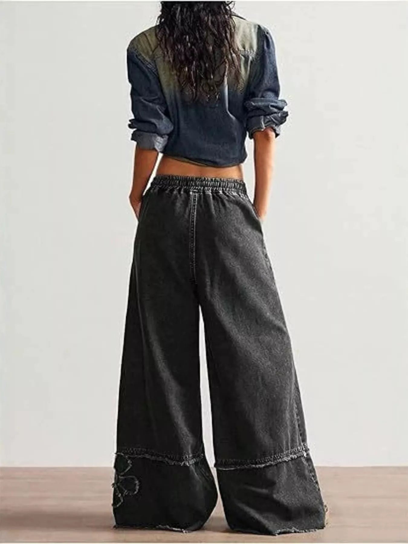 Wide-leg denim pants with drawstring waist, pockets, raw hem details, seam accents, and distressed floral appliqué designs.