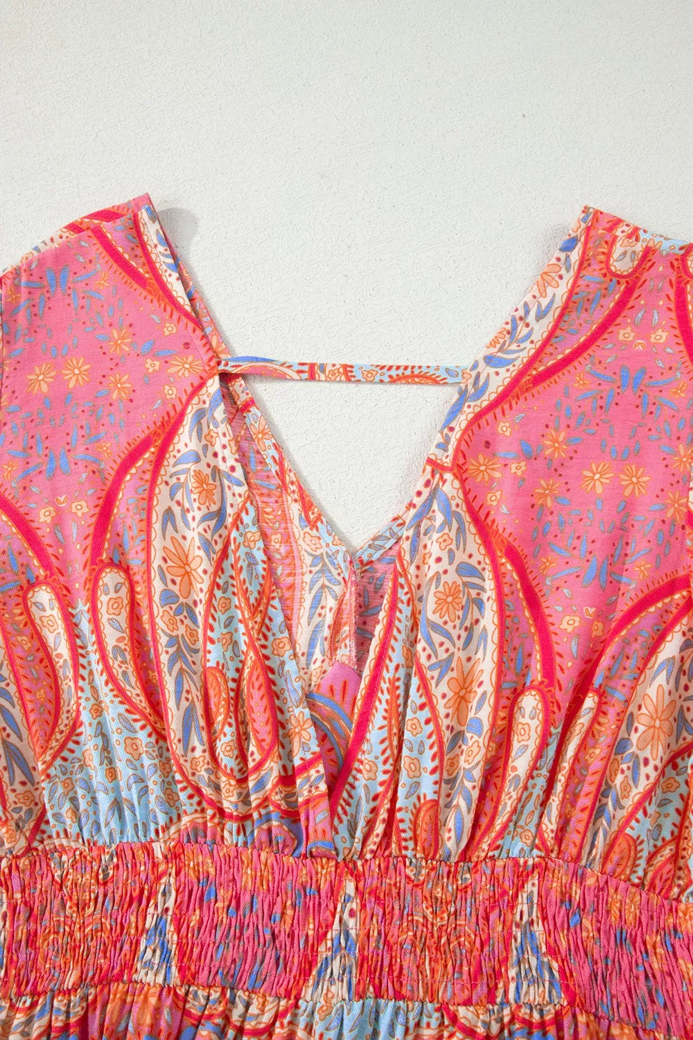 Pink paisley tiered midi dress with V-neckline, flutter sleeves, flowy silhouette, and slightly stretchy fabric styled with heels and a woven bag.