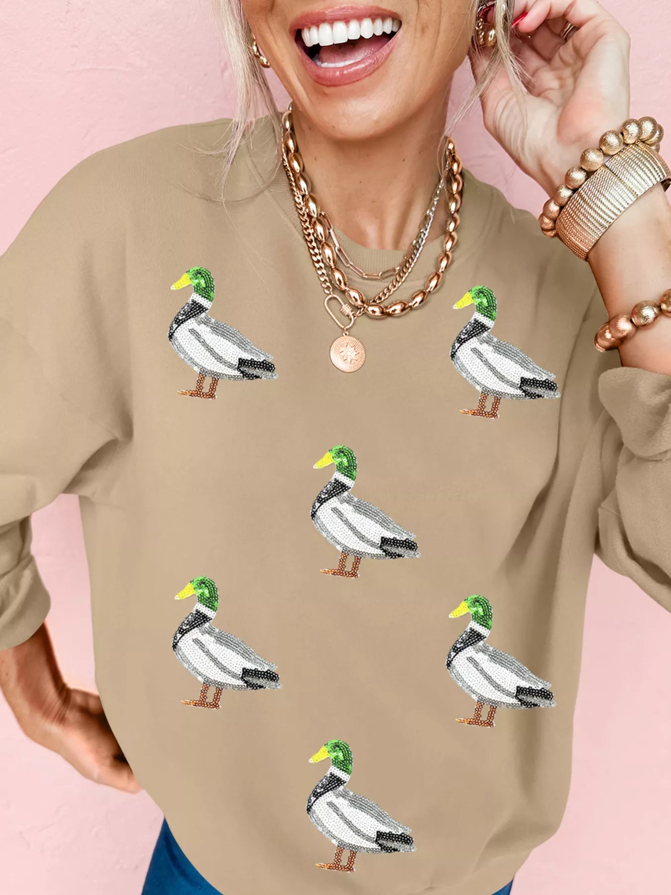Woman wearing tan Duckie Sparkle Sweatshirt with sequin duck designs, fun quirky casual top for animal lovers.