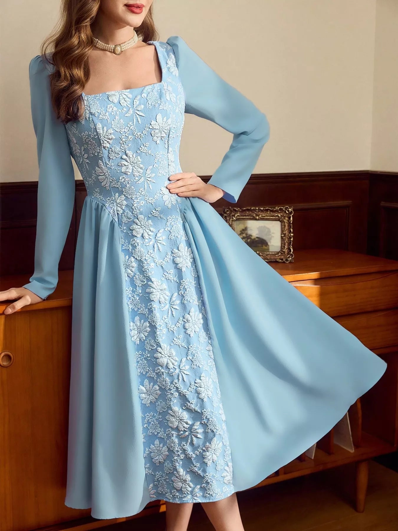 Woman wearing a light blue midi dress with long sleeves, square neckline, and white floral embroidery on the front panel.