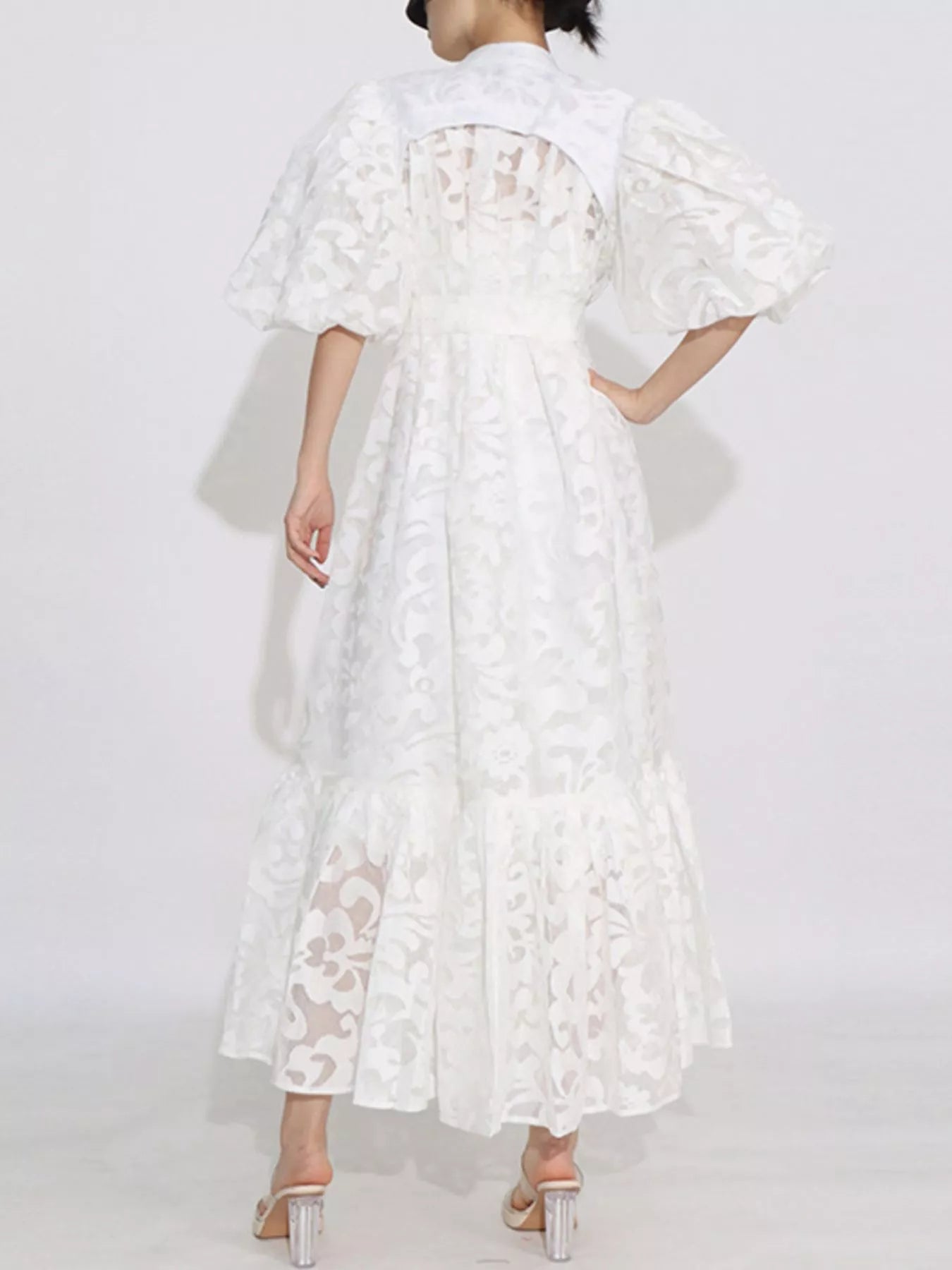 Model wearing the Ethereal Grace Lace Maxi Dress in white, featuring puff sleeves, button-down front, tie waist, and sheer lace detail.