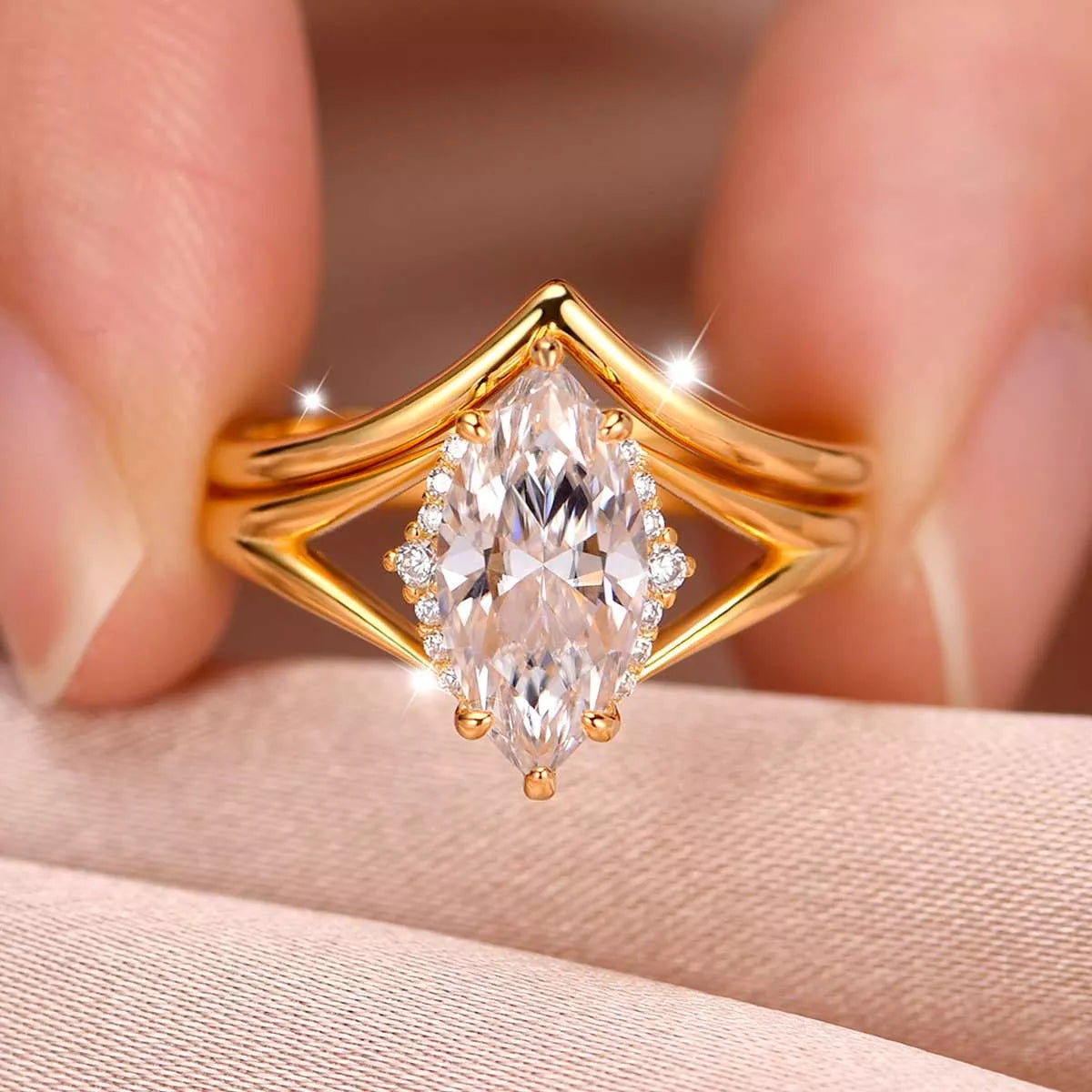 Gold two-piece marquise-cut moissanite ring set with a heart-shaped curved band displayed in a blush jewelry box.