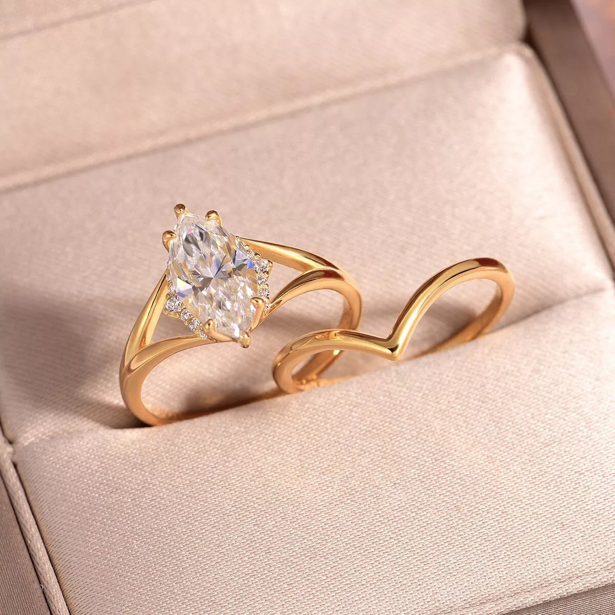 Gold two-piece marquise-cut moissanite ring set with a heart-shaped curved band displayed in a blush jewelry box.