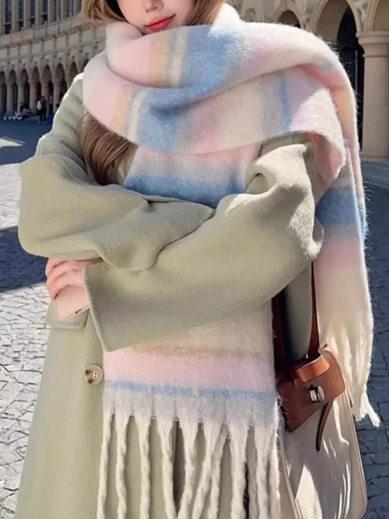 Oversized soft fringe scarf in pastel gradient tones, worn layered as a winter wrap.