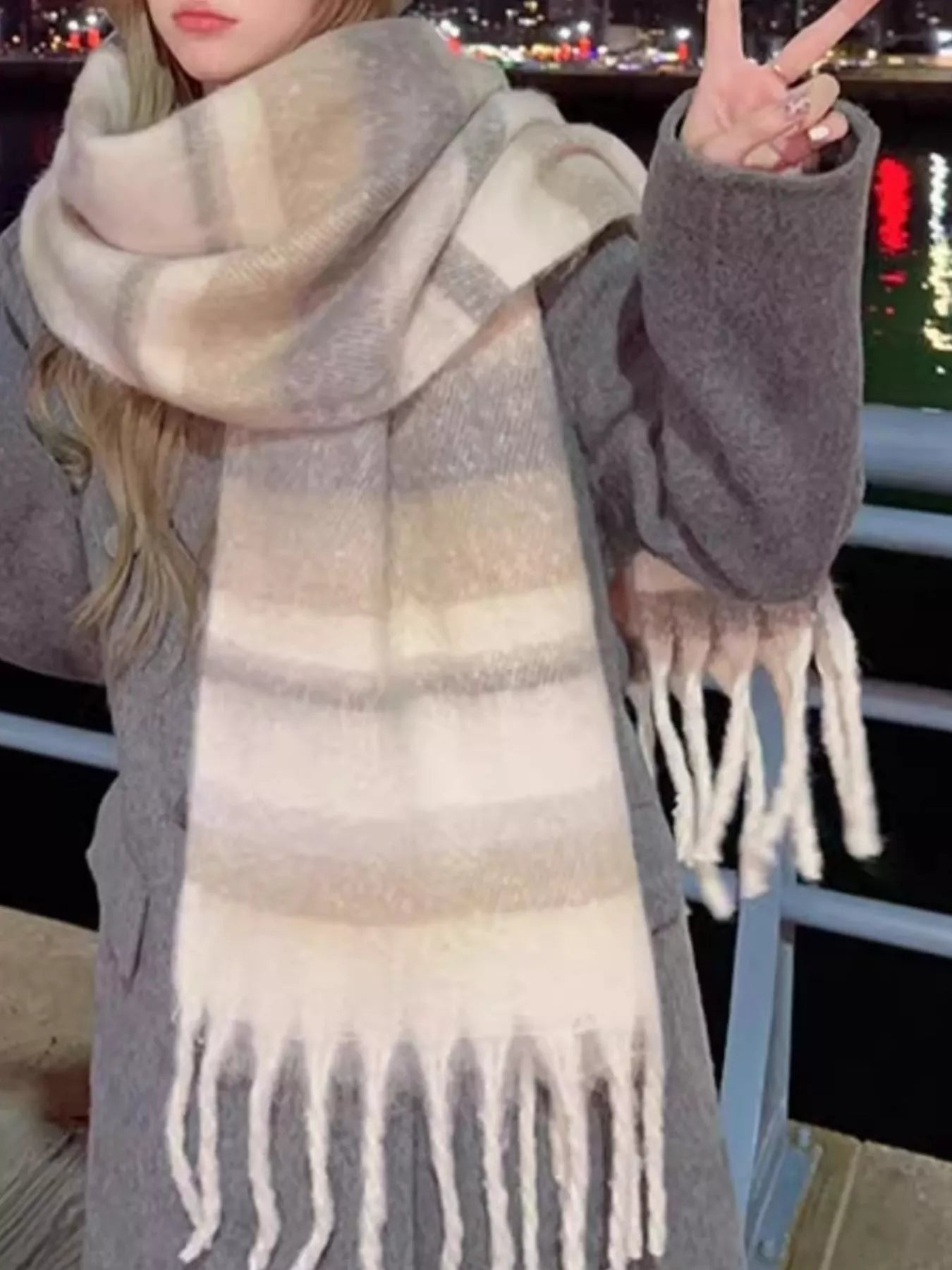 Oversized soft fringe scarf in pastel gradient tones, worn layered as a winter wrap.