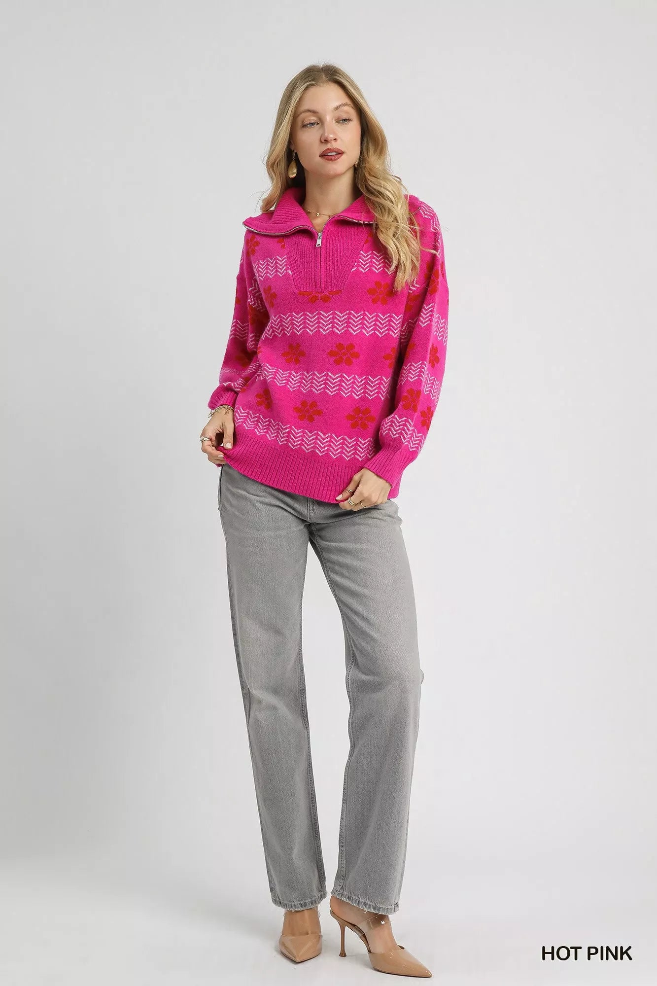 Woman wearing a hot pink floral and chevron jacquard quarter-zip sweater with ribbed cuffs and hem, paired with light grey jeans.