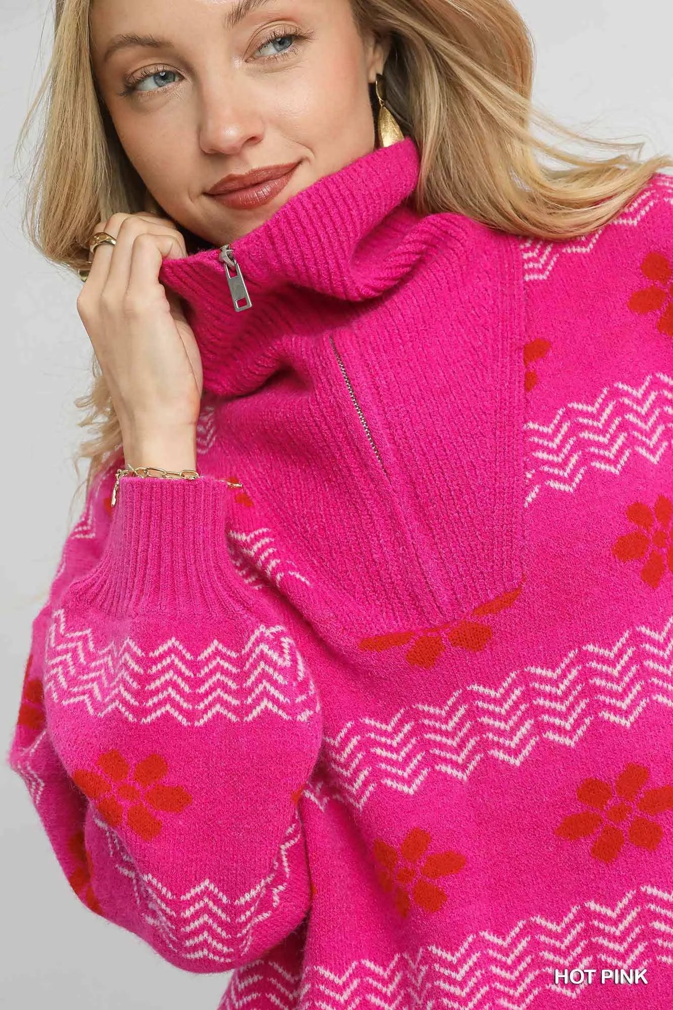 Woman wearing a hot pink floral and chevron jacquard quarter-zip sweater with ribbed cuffs and hem, paired with light grey jeans.