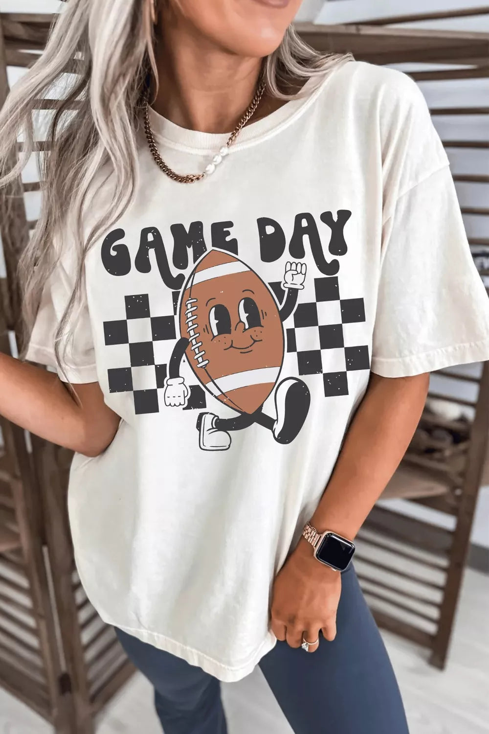 White graphic tee with bold “Game Day” text, a smiling football illustration, and black checkerboard accents.