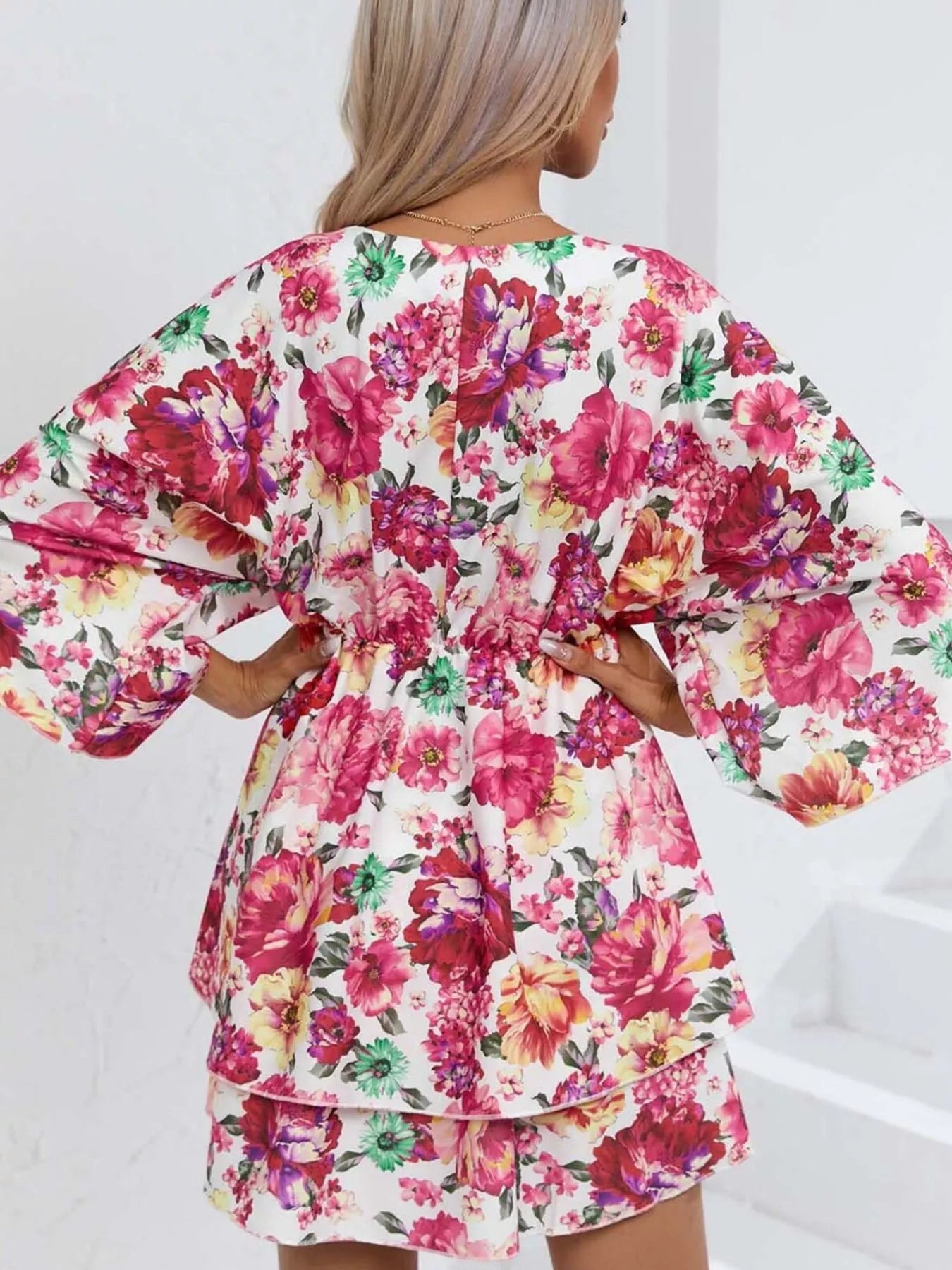 Floral mini dress with a surplice V-neckline, flowy sleeves, tiered skirt, and bright pink floral print.