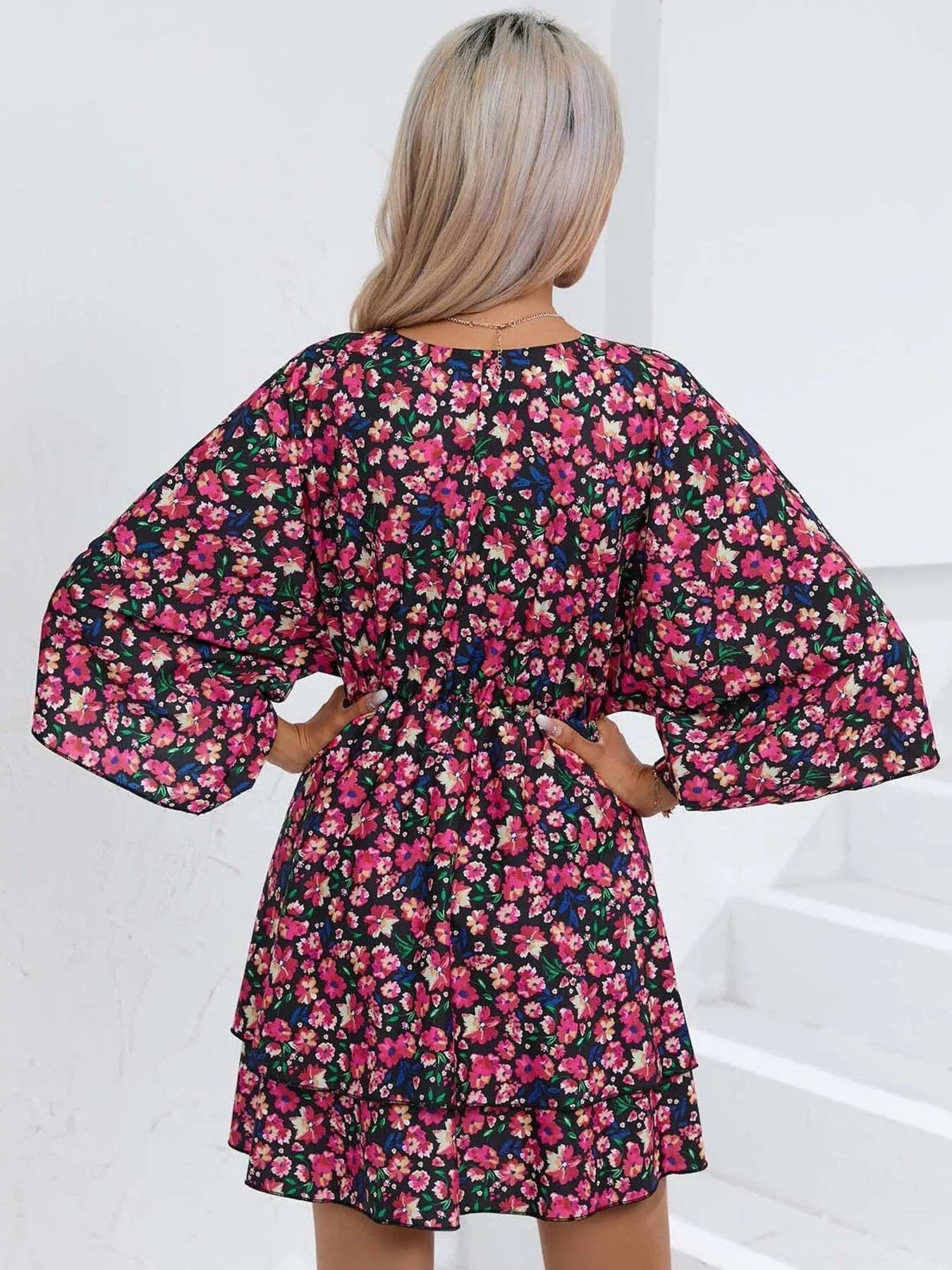 Floral mini dress with a surplice V-neckline, flowy sleeves, tiered skirt, and bright pink floral print.
