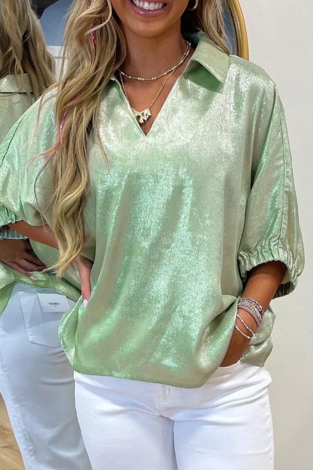 Shimmery collared puff sleeve top with a split neckline, relaxed fit, and satin-like finish styled with white pants.