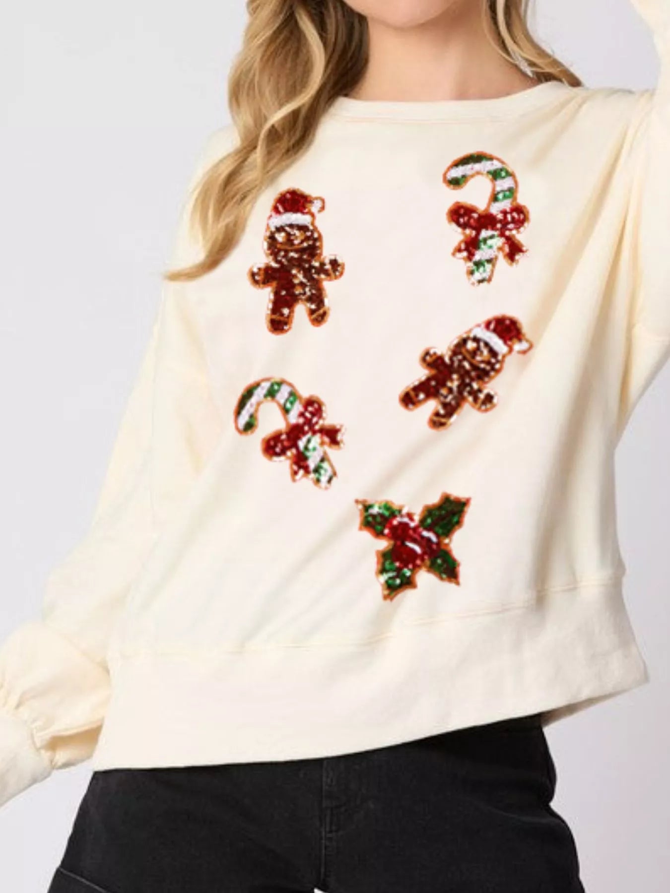 Woman wearing a cream sweatshirt with sequin gingerbread men and candy canes — cozy holiday pullover.