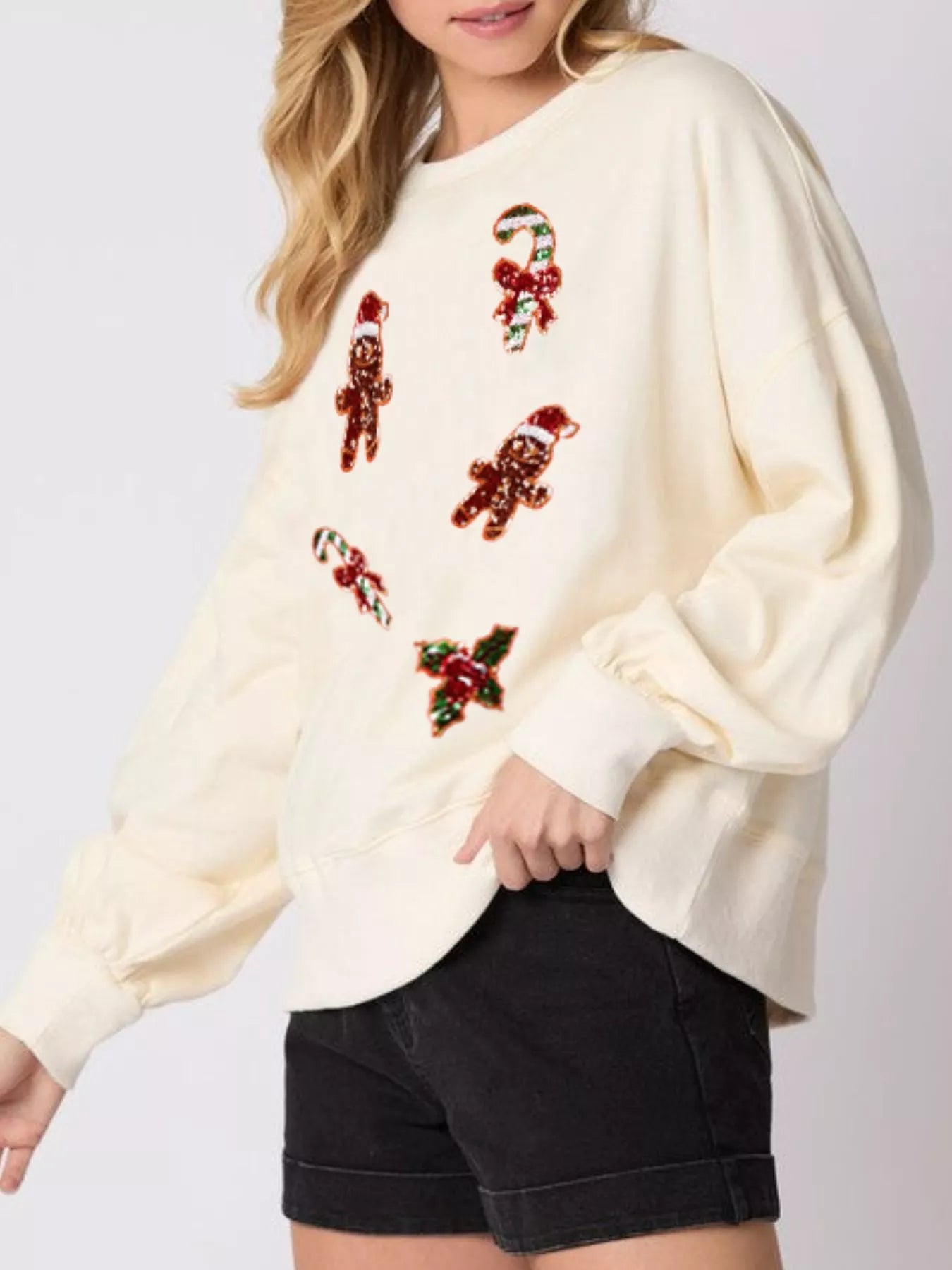 Woman wearing a cream sweatshirt with sequin gingerbread men and candy canes — cozy holiday pullover.