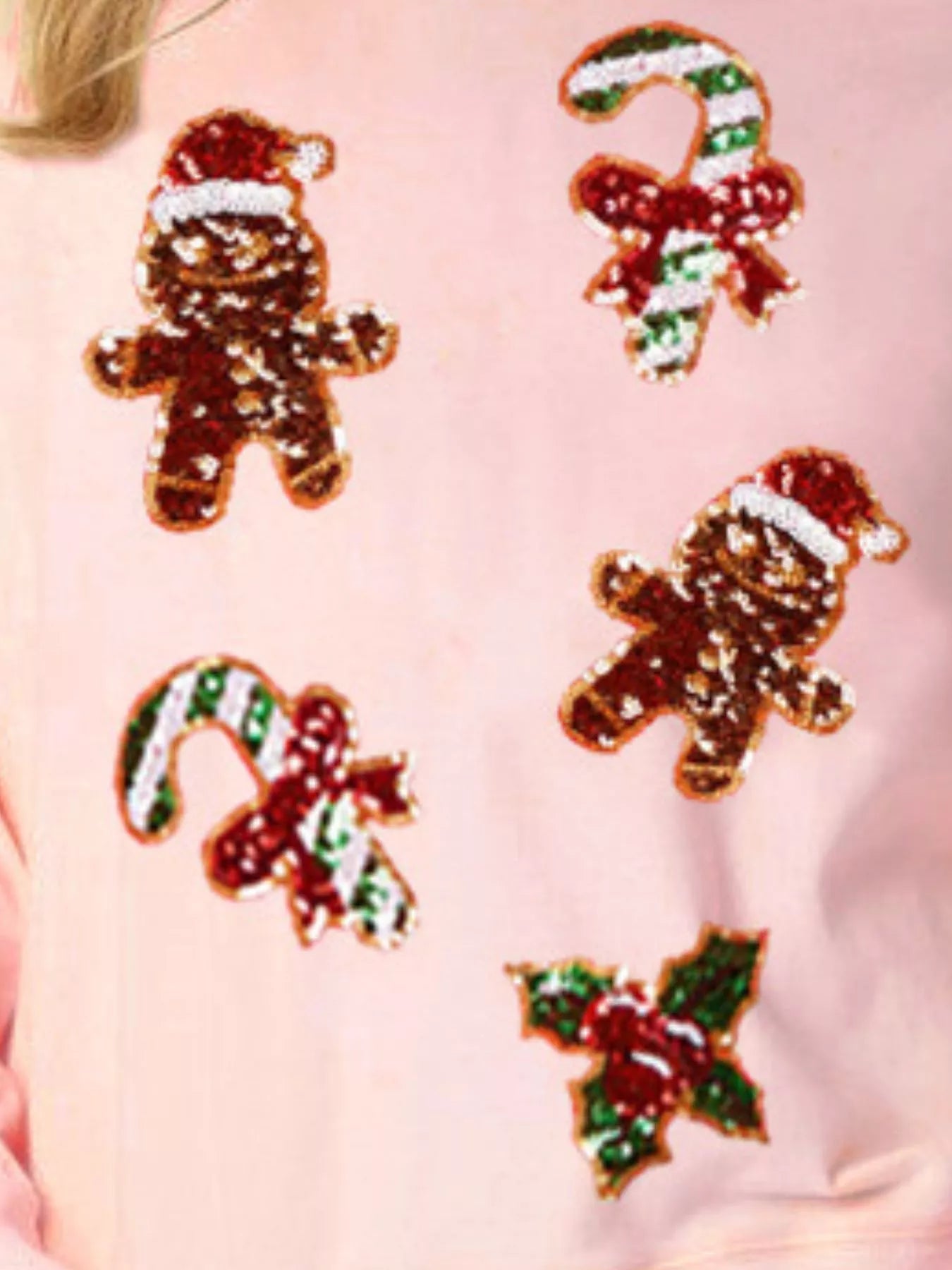 Woman wearing a pink sweatshirt with sequin gingerbread men, candy canes, and holly — festive Christmas top from A Whimsical Affair.