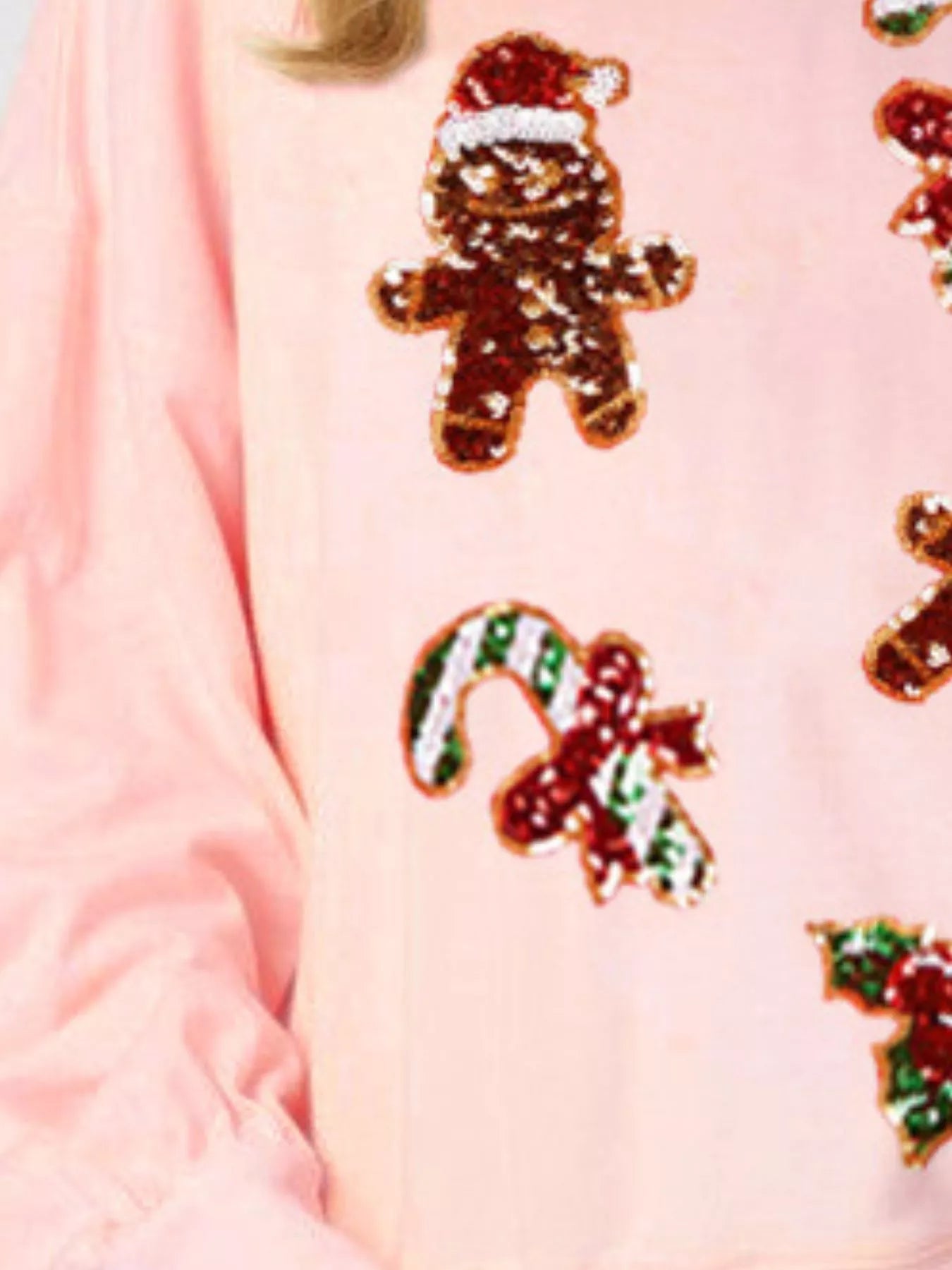 Woman wearing a pink sweatshirt with sequin gingerbread men, candy canes, and holly — festive Christmas top from A Whimsical Affair.