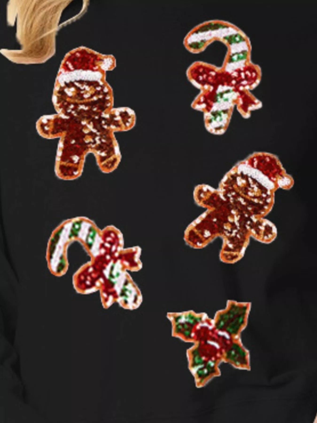 Woman wearing a black sweatshirt with colorful sequin gingerbread designs — sparkly festive top for Christmas.