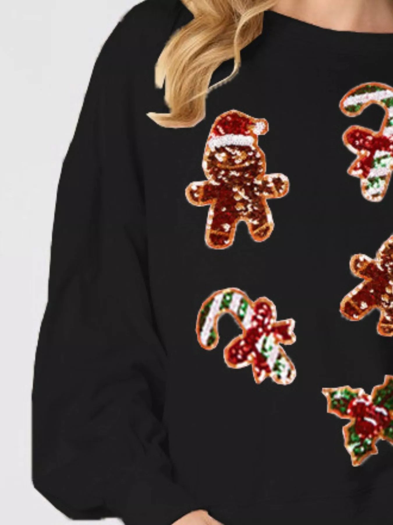 Woman wearing a black sweatshirt with colorful sequin gingerbread designs — sparkly festive top for Christmas.