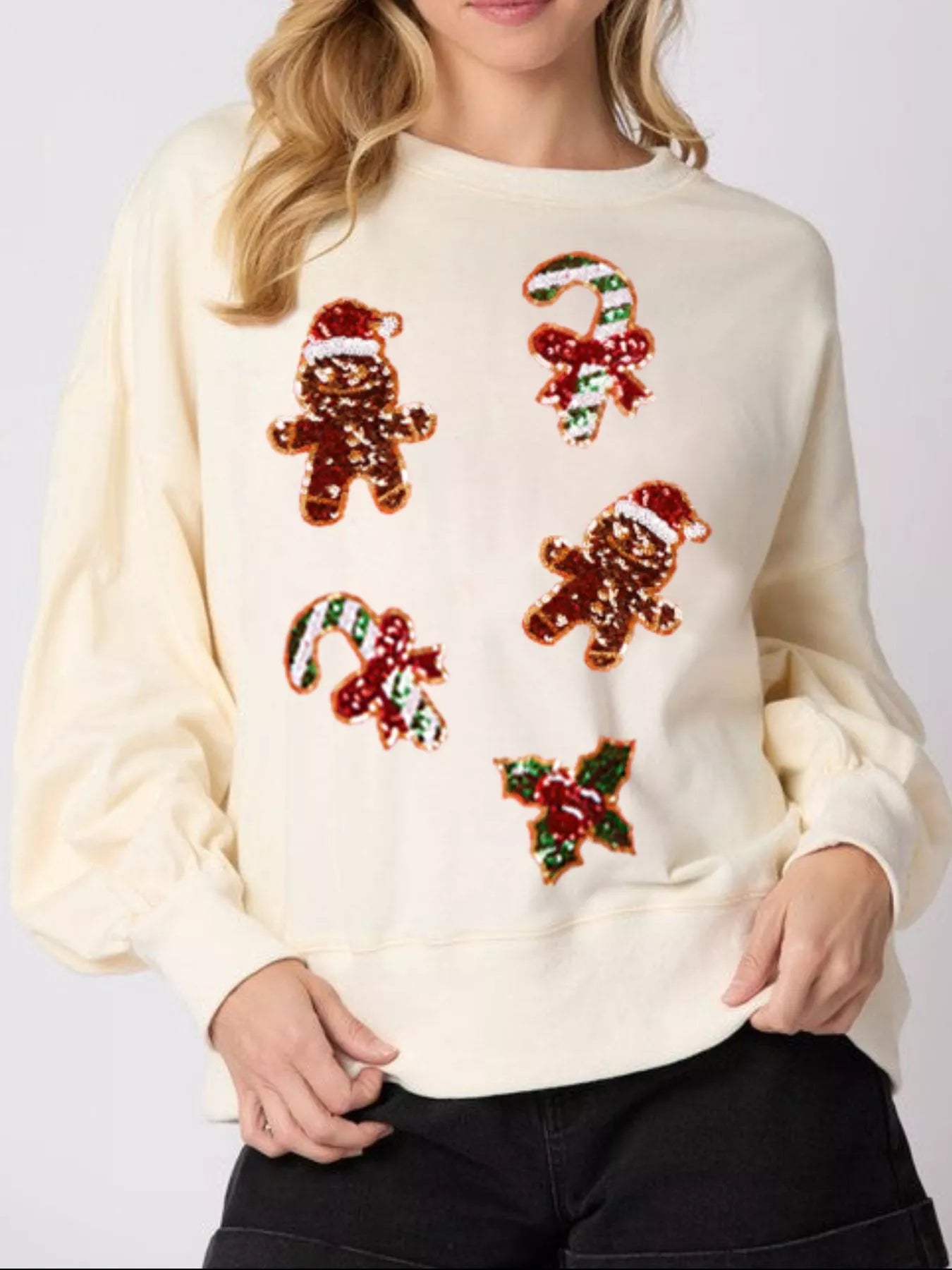 Woman wearing a cream sweatshirt with sequin gingerbread men and candy canes — cozy holiday pullover.