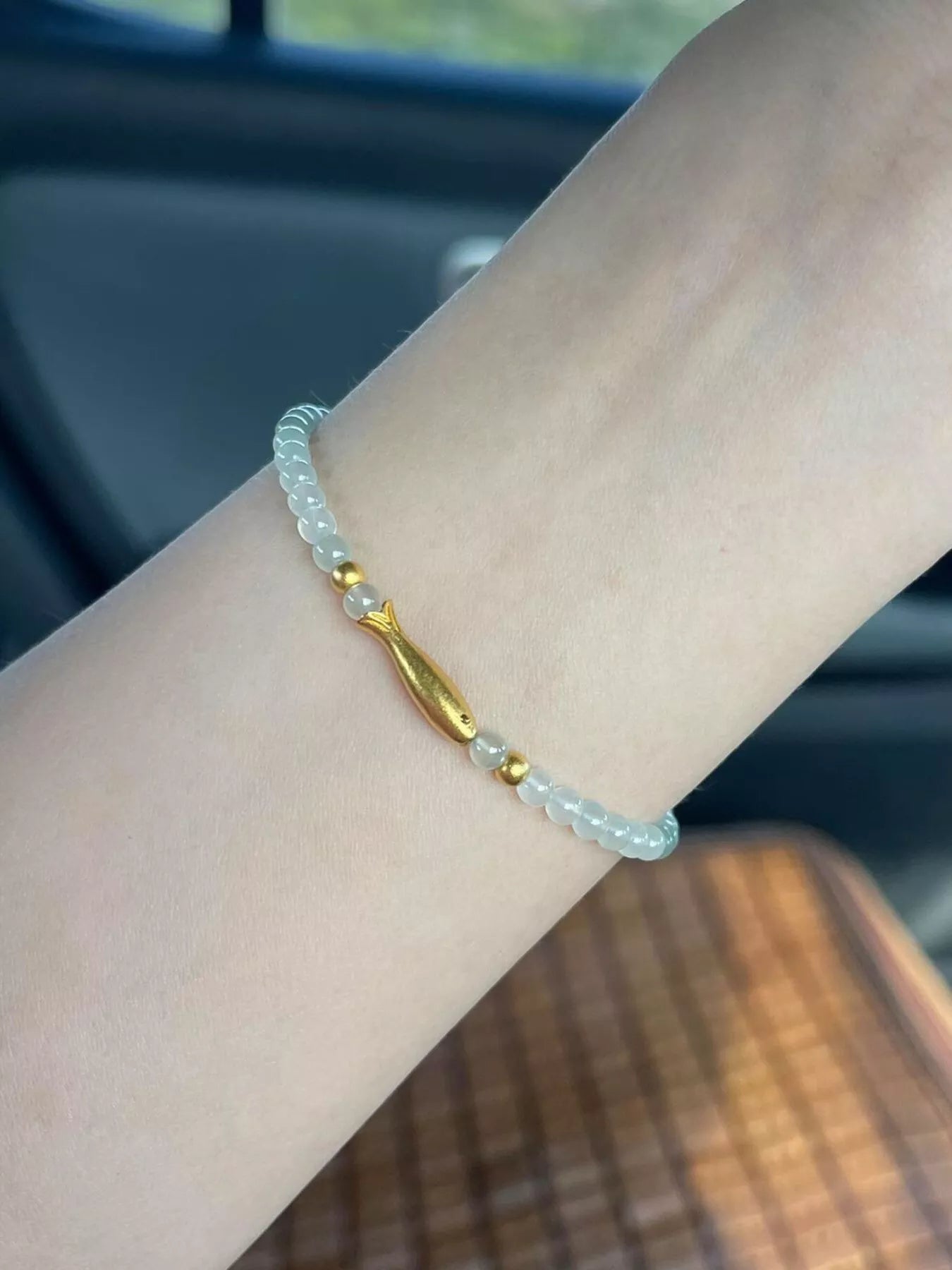 Dainty beaded bracelet with pale glass beads, 18K gold-plated accents, and a gold fish charm worn on the wrist.