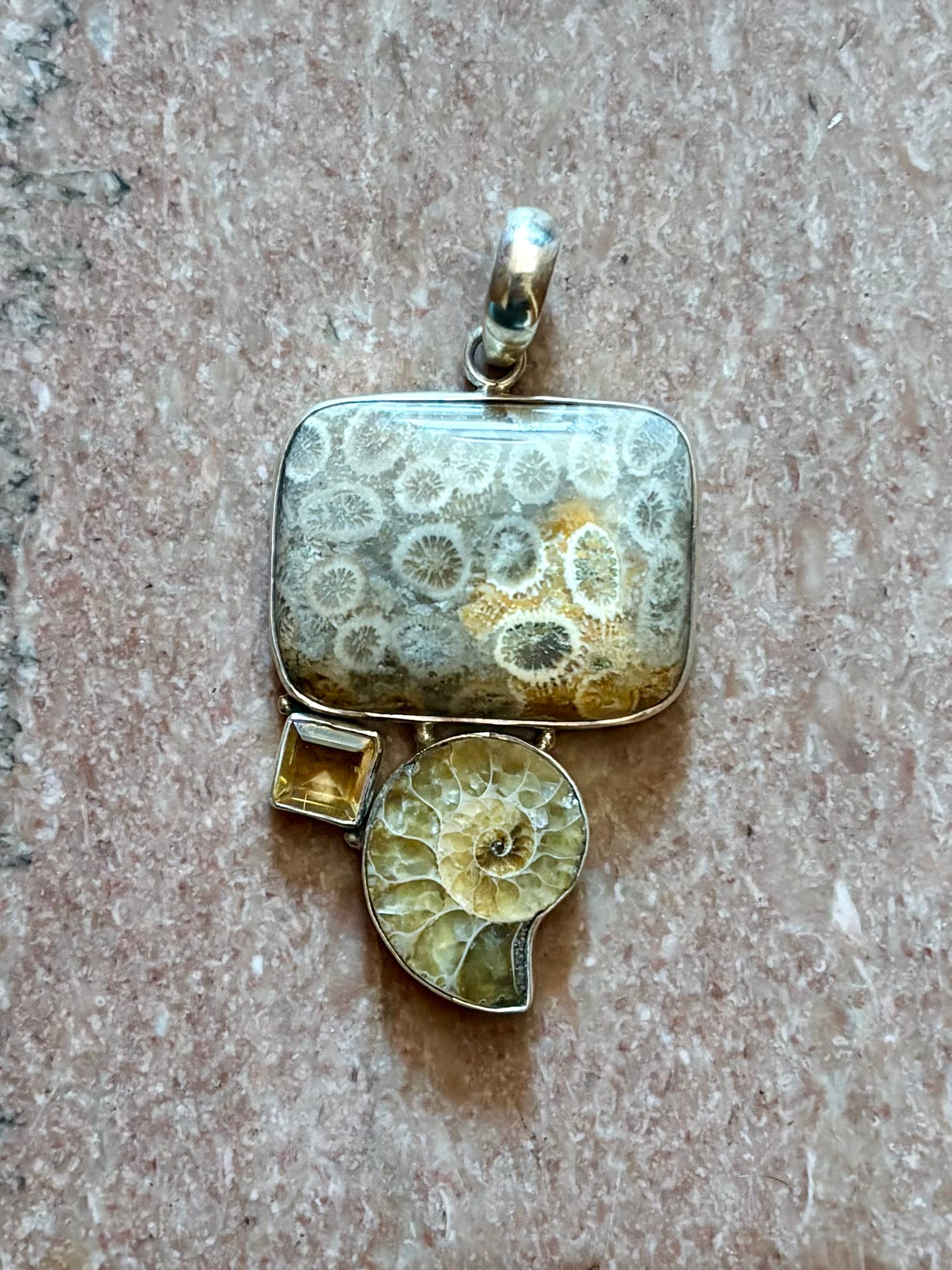 Silver pendant with a rectangular fossilized material and round ammonite fossil on a brown surface