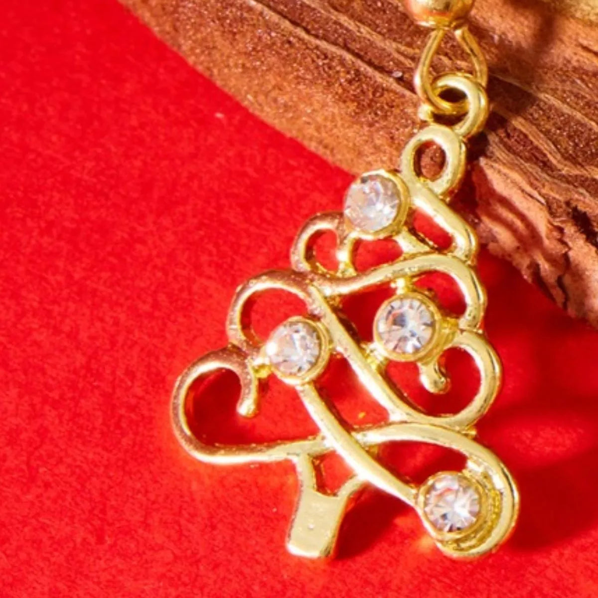 Gold Christmas tree-shaped earrings with rhinestone accents hanging on a gold display bar against a red background.