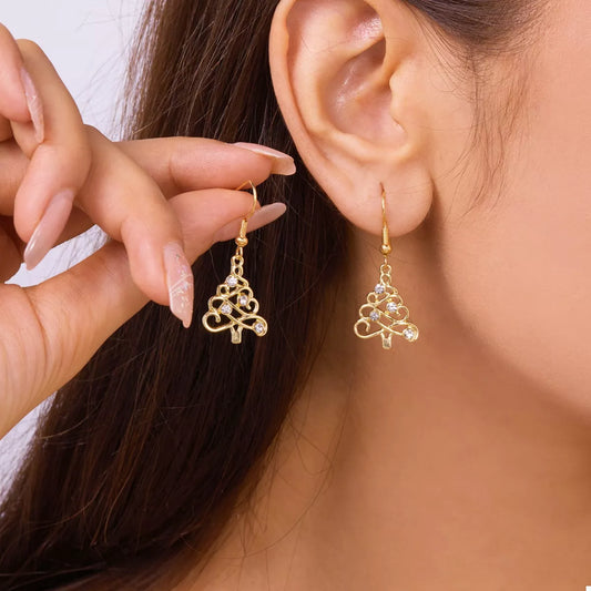 Gold Christmas tree-shaped earrings with rhinestone accents hanging on a gold display bar against a red background.