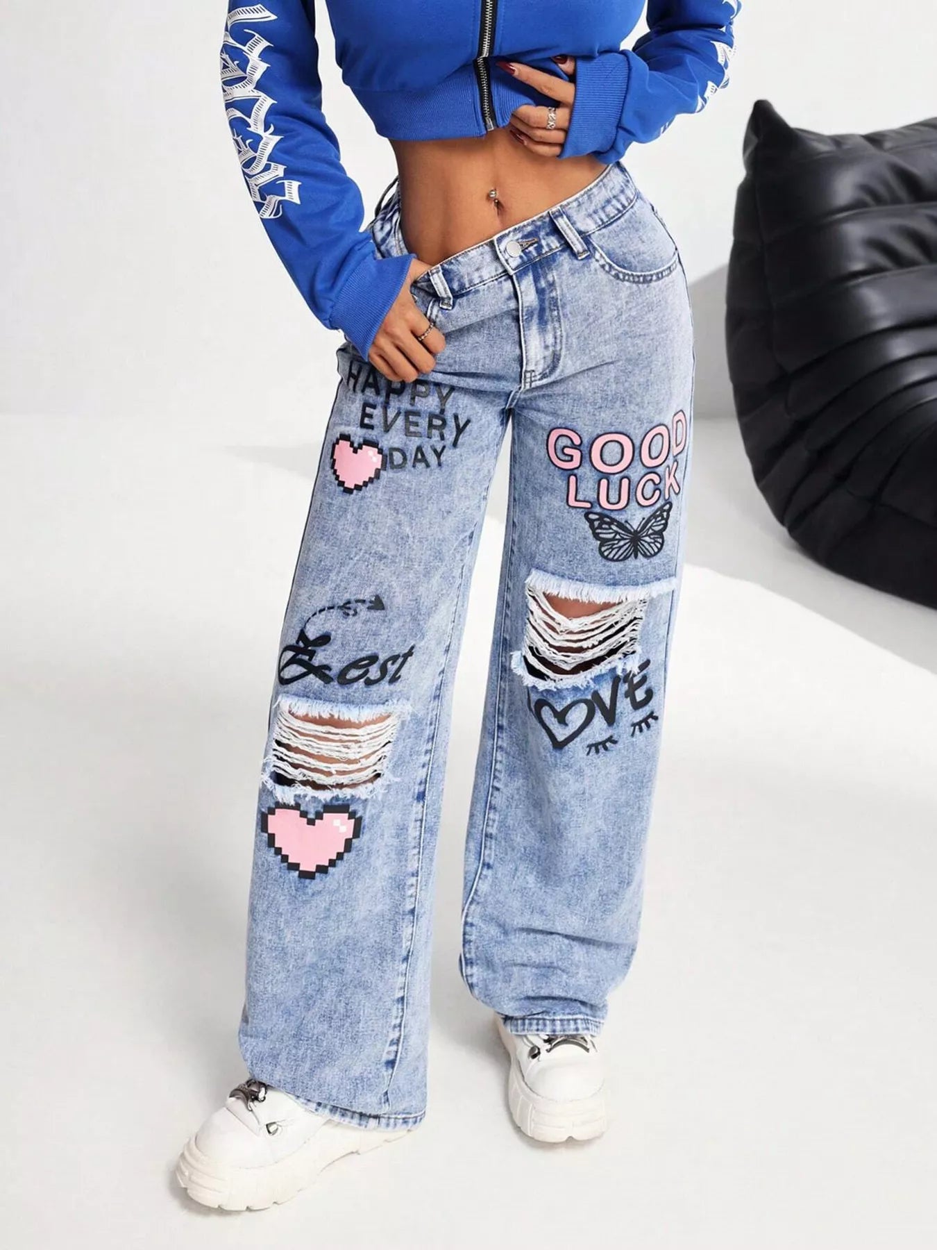 Light wash wide-leg jeans with distressed cutouts, graphic lettering, butterfly detail, and relaxed street-style fit.
