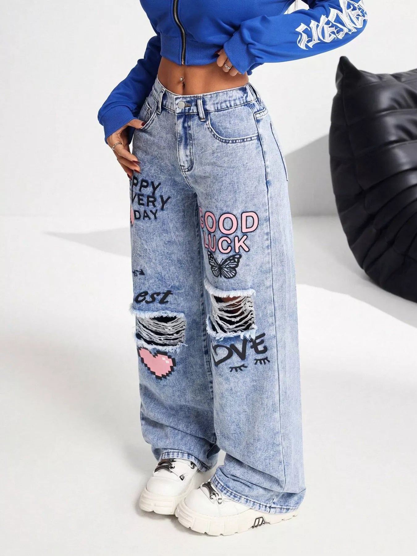 Light wash wide-leg jeans with distressed cutouts, graphic lettering, butterfly detail, and relaxed street-style fit.