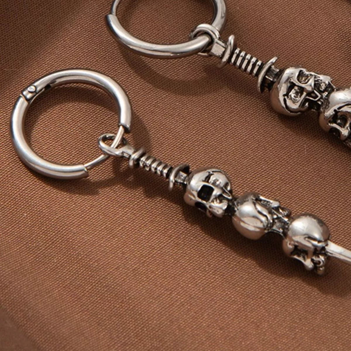 Close-up of silver skull drop earrings with stacked skull design hanging from small hoops — gothic Halloween jewelry from A Whimsical Affair.