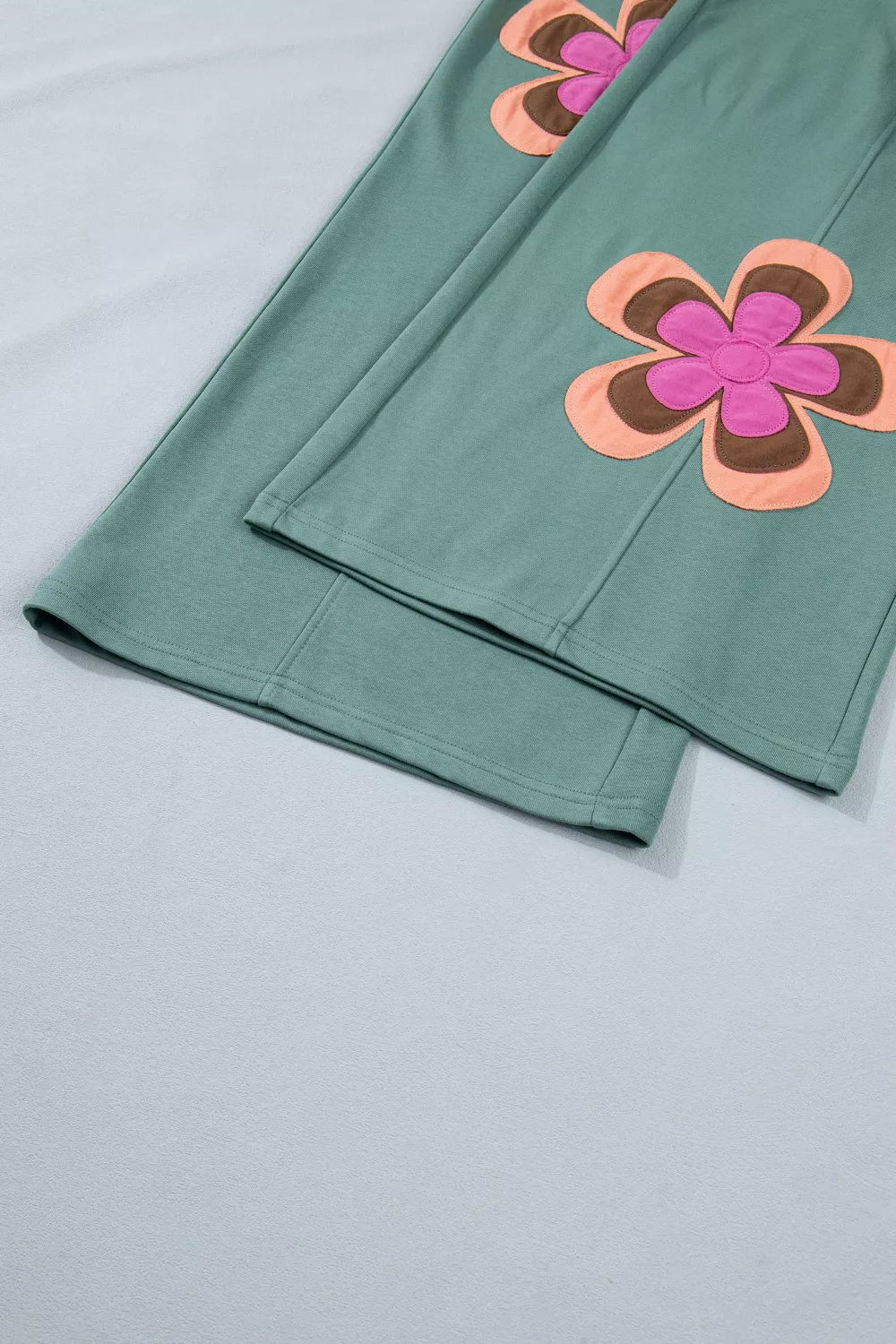 Teal wide-leg sweatpants with drawstring waist, front pockets, and colorful floral appliqué details.