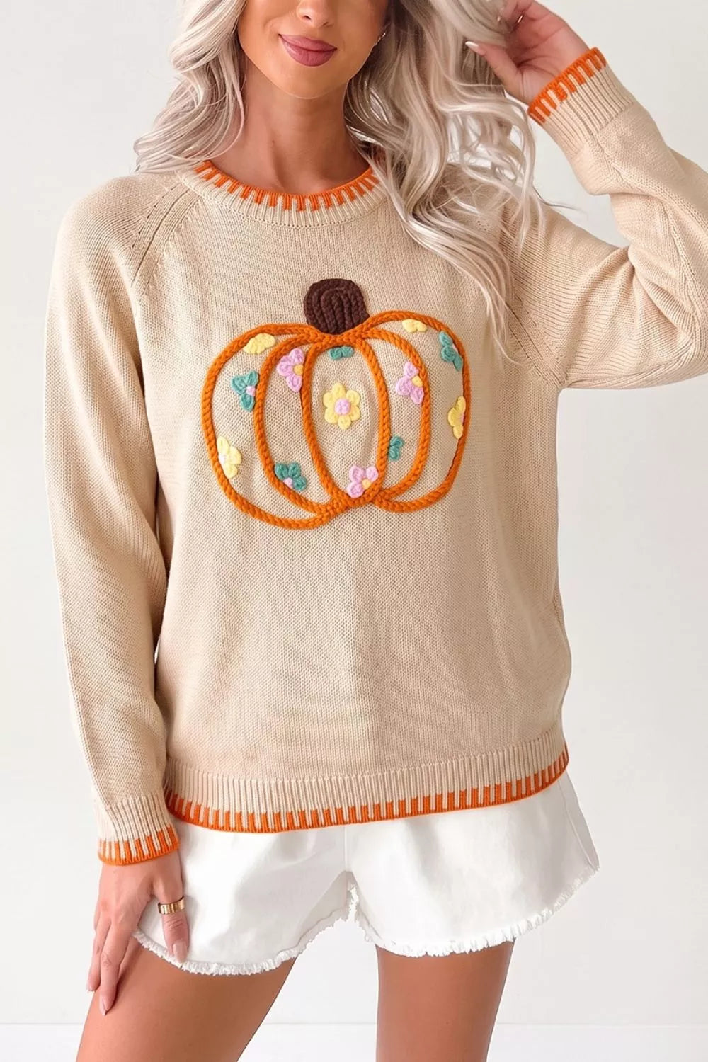 Cream knit sweater with embroidered pumpkin design, tiny floral accents, orange trim, seam details, and slightly stretchy fabric.
