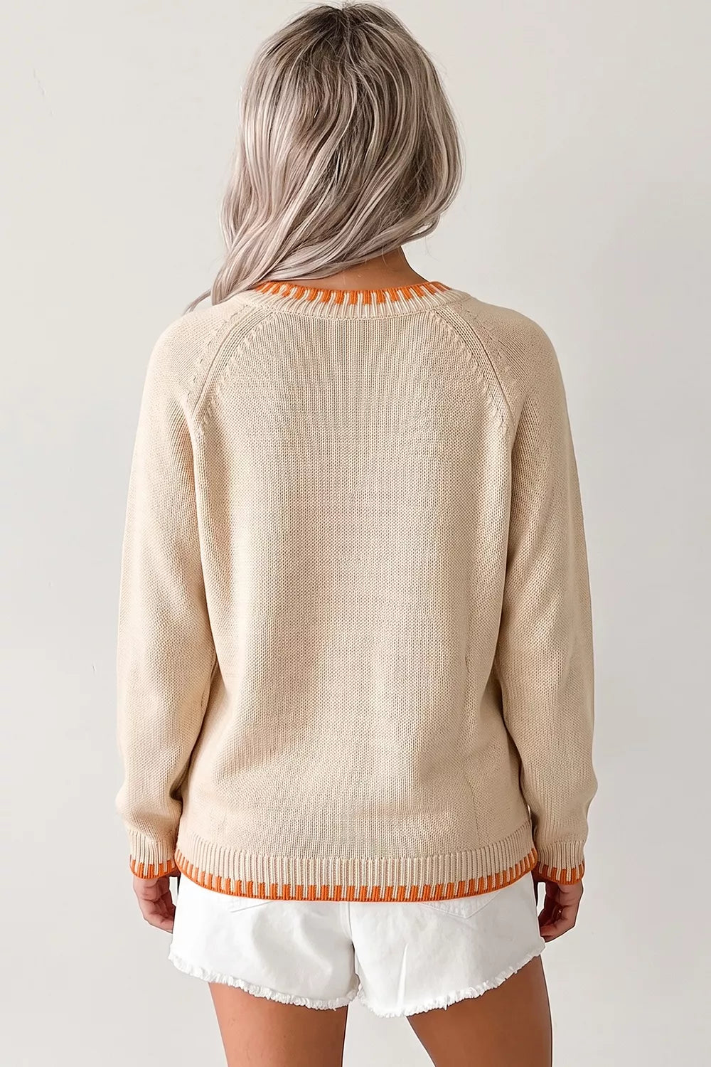 Cream knit sweater with embroidered pumpkin design, tiny floral accents, orange trim, seam details, and slightly stretchy fabric.