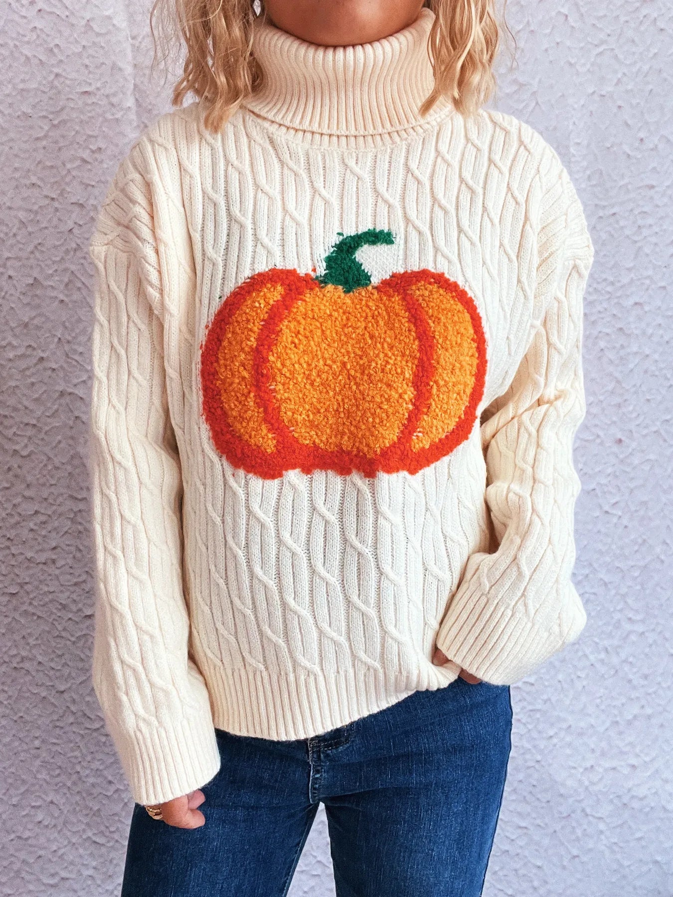 Woman wearing cream cable-knit turtleneck sweater with orange pumpkin applique — cozy fall fashion from A Whimsical Affair.