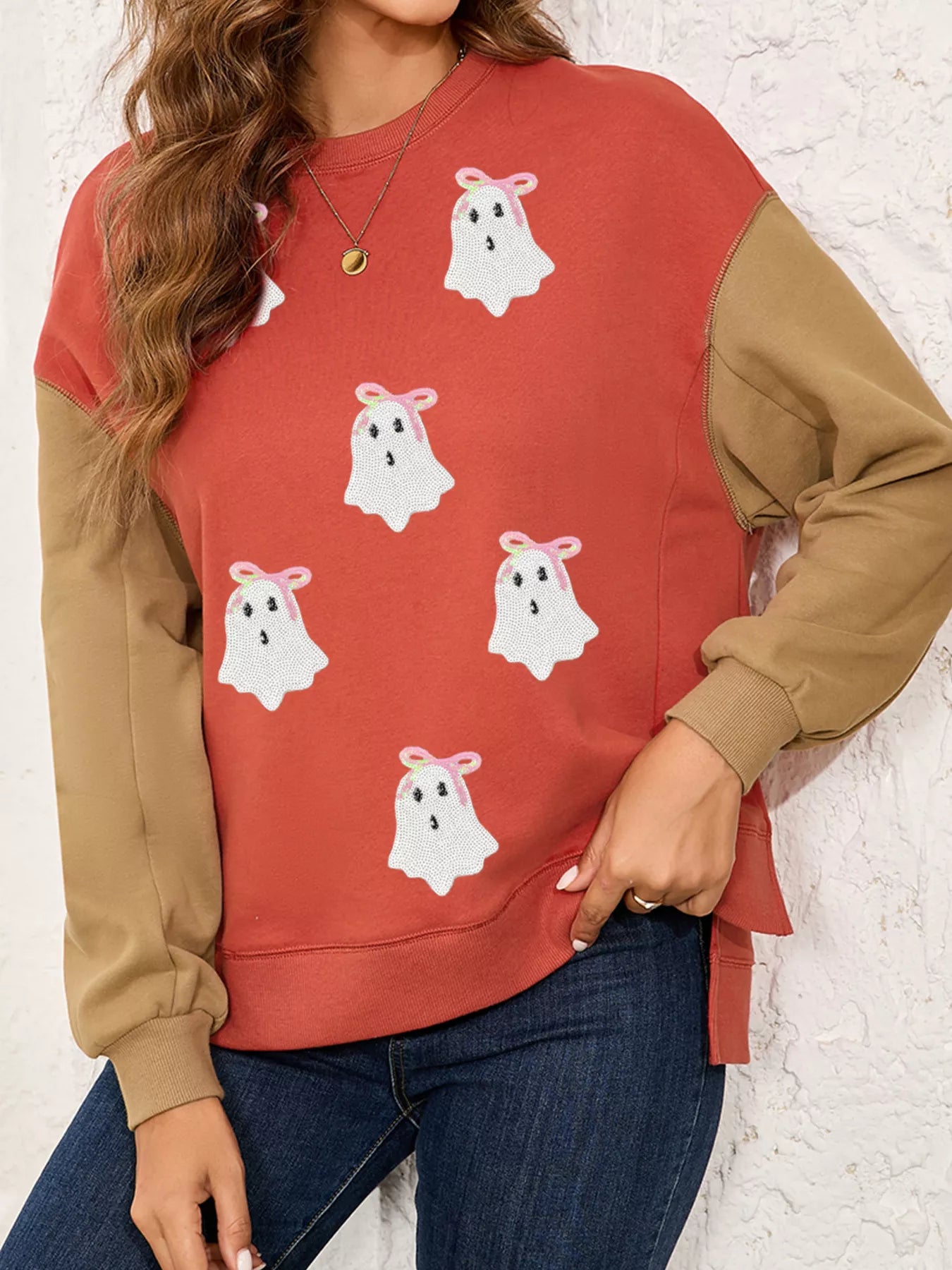 Woman wearing a rust-orange sweatshirt with sequin white ghosts topped with pink bows — festive and cozy Halloween top from A Whimsical Affair.