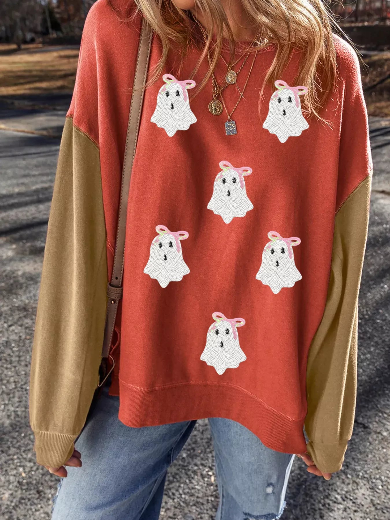 Woman wearing a rust-orange sweatshirt with sequin white ghosts topped with pink bows — festive and cozy Halloween top from A Whimsical Affair.