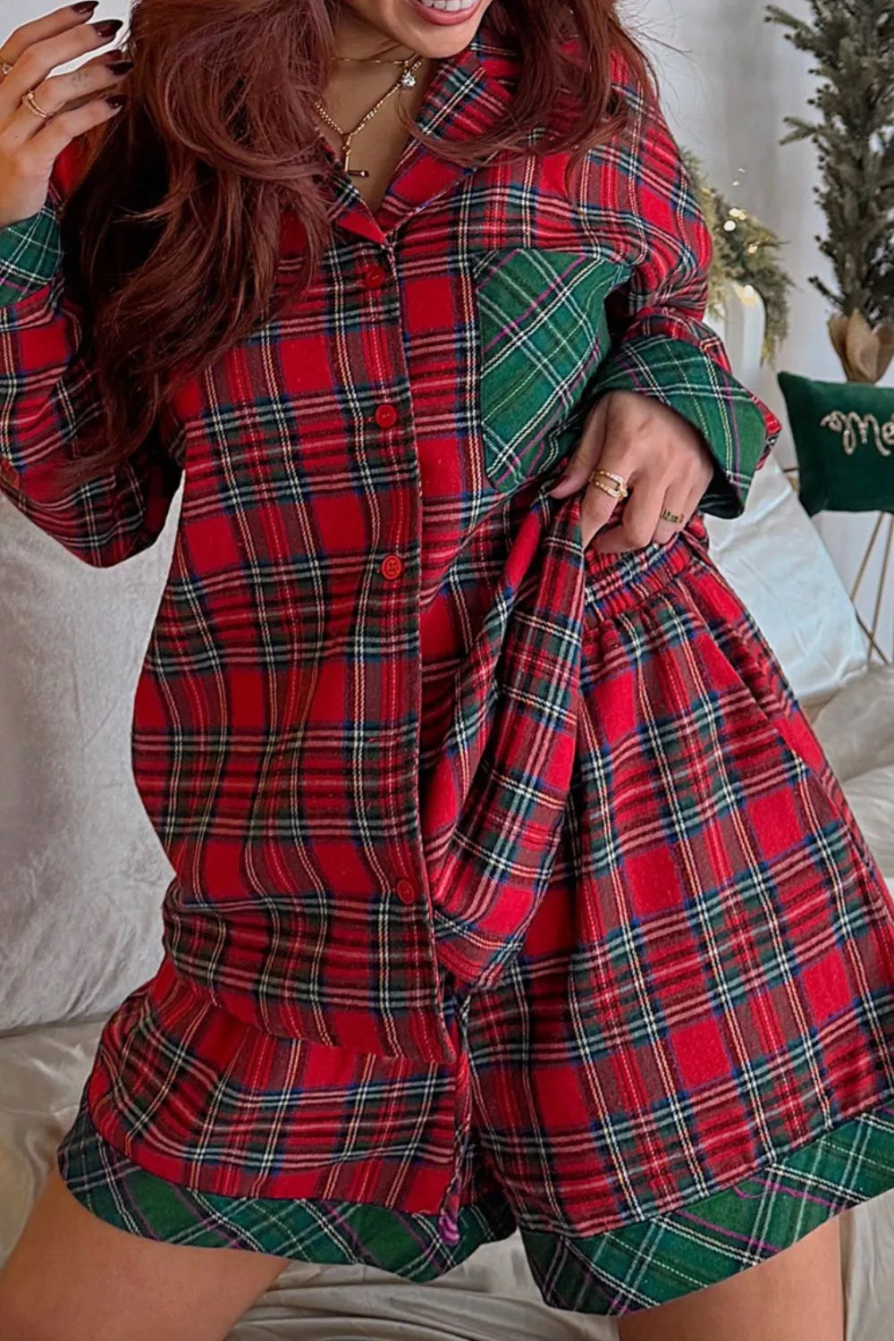 Model wearing red plaid button-down pajama set with green contrast pocket and shorts.