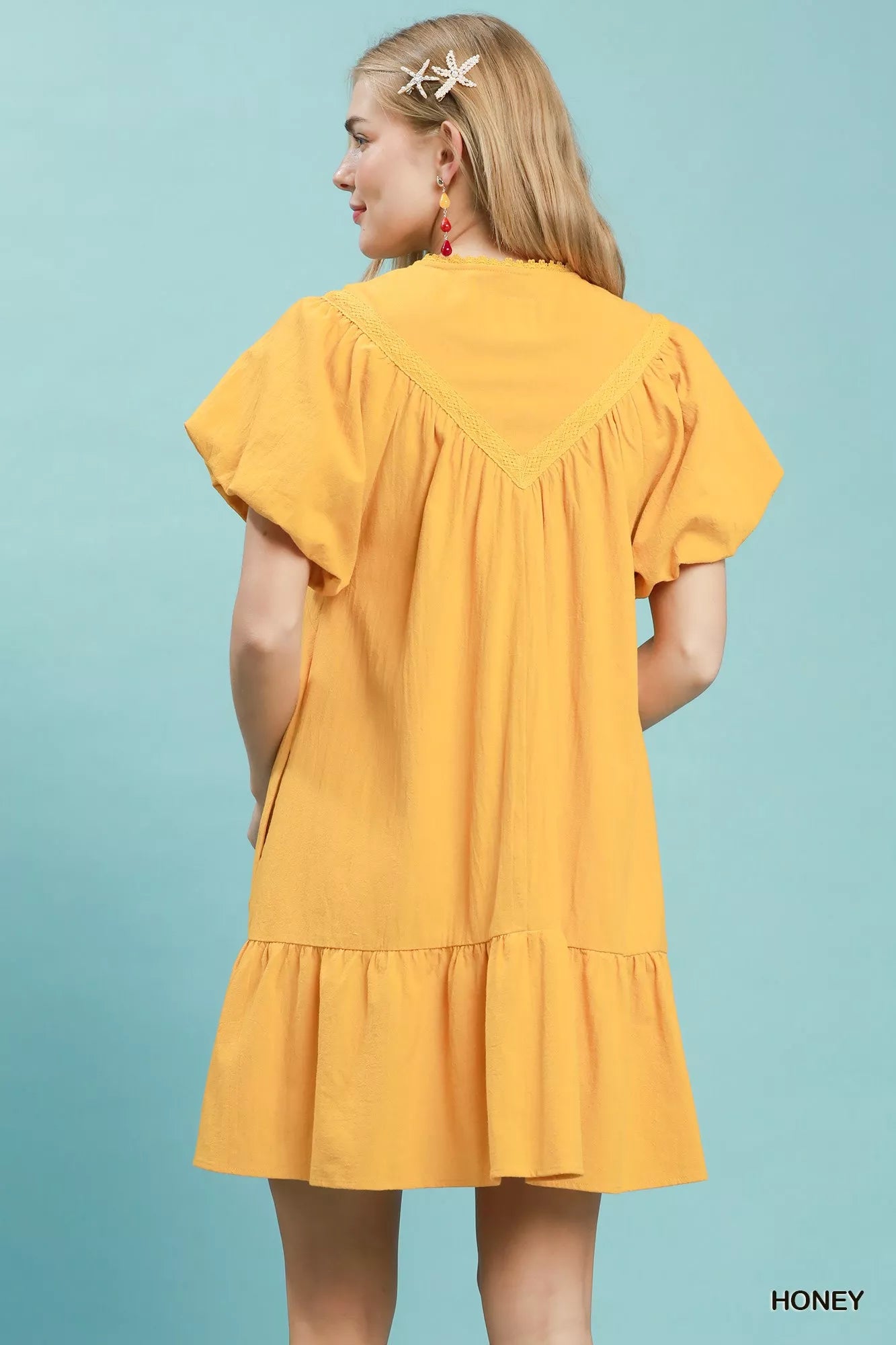 Honey yellow cotton mini dress with split V-neckline, tassel tie detail, flutter sleeves, ruffled hem, and side pockets.