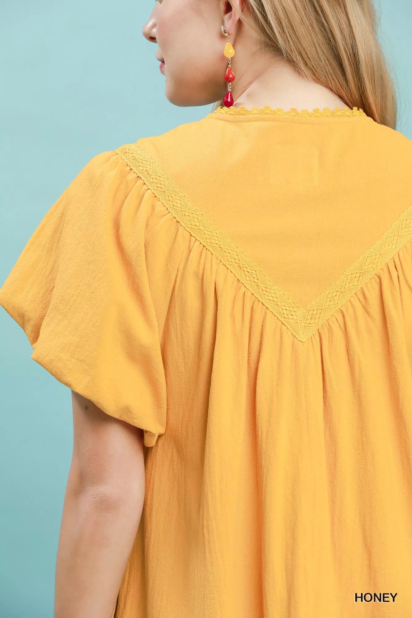 Honey yellow cotton mini dress with split V-neckline, tassel tie detail, flutter sleeves, ruffled hem, and side pockets.