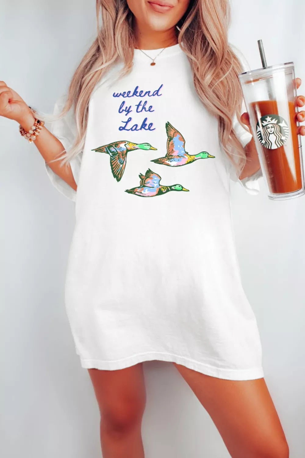 White graphic tee with “weekend by the lake” text and colorful flying duck design on the front.