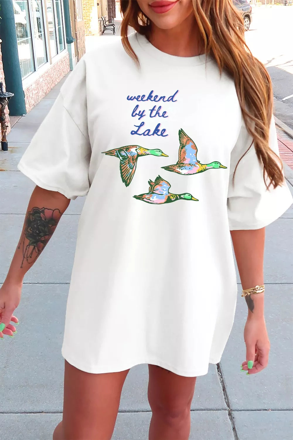White graphic tee with “weekend by the lake” text and colorful flying duck design on the front.