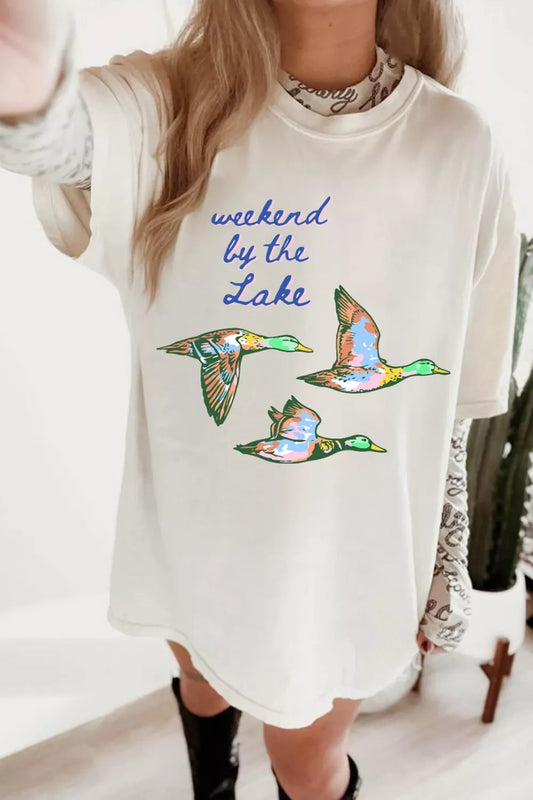 White graphic tee with “weekend by the lake” text and colorful flying duck design on the front.