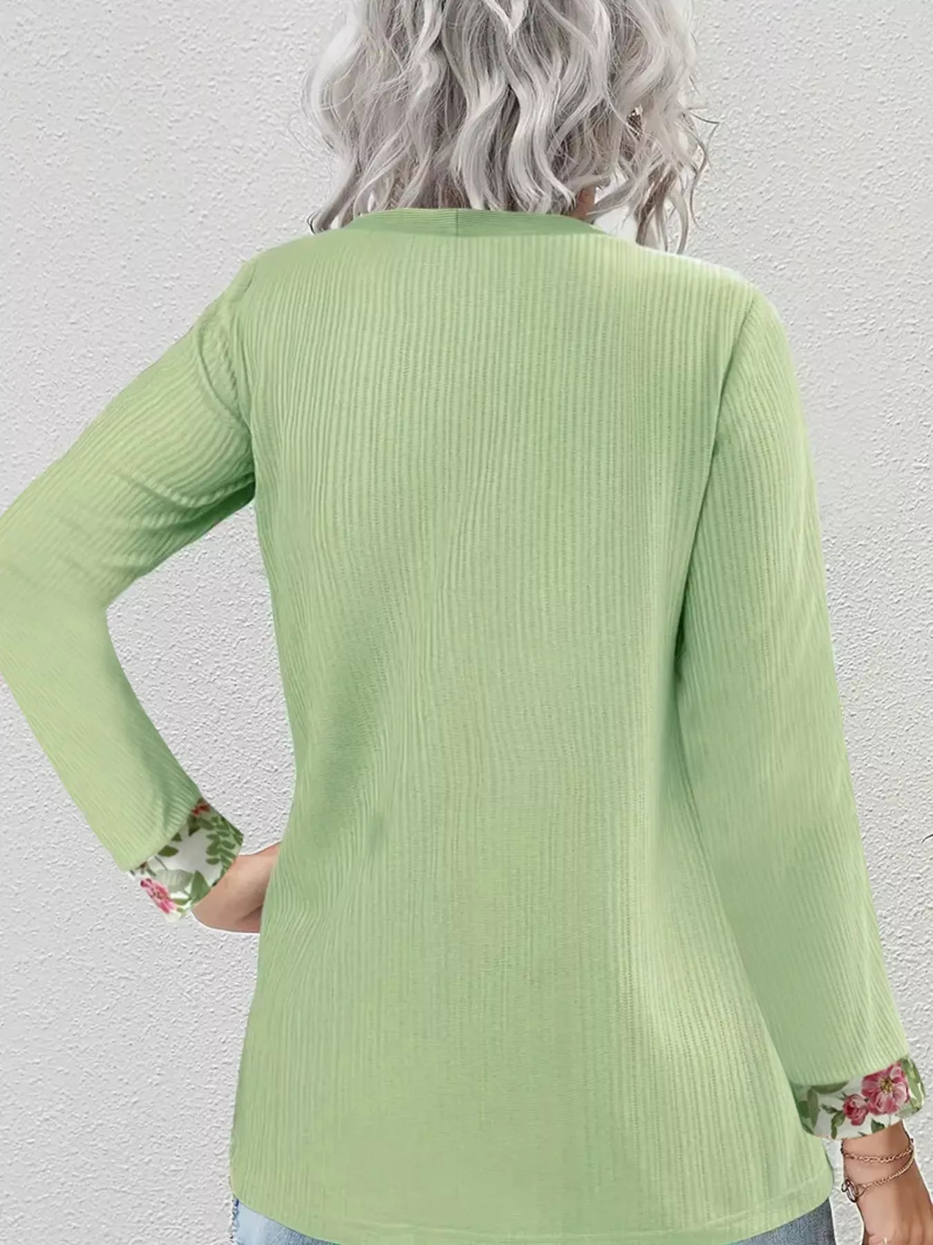 Woman wearing a faux two-piece top with a ribbed outer layer and floral underlayer at the neckline and sleeve cuffs.