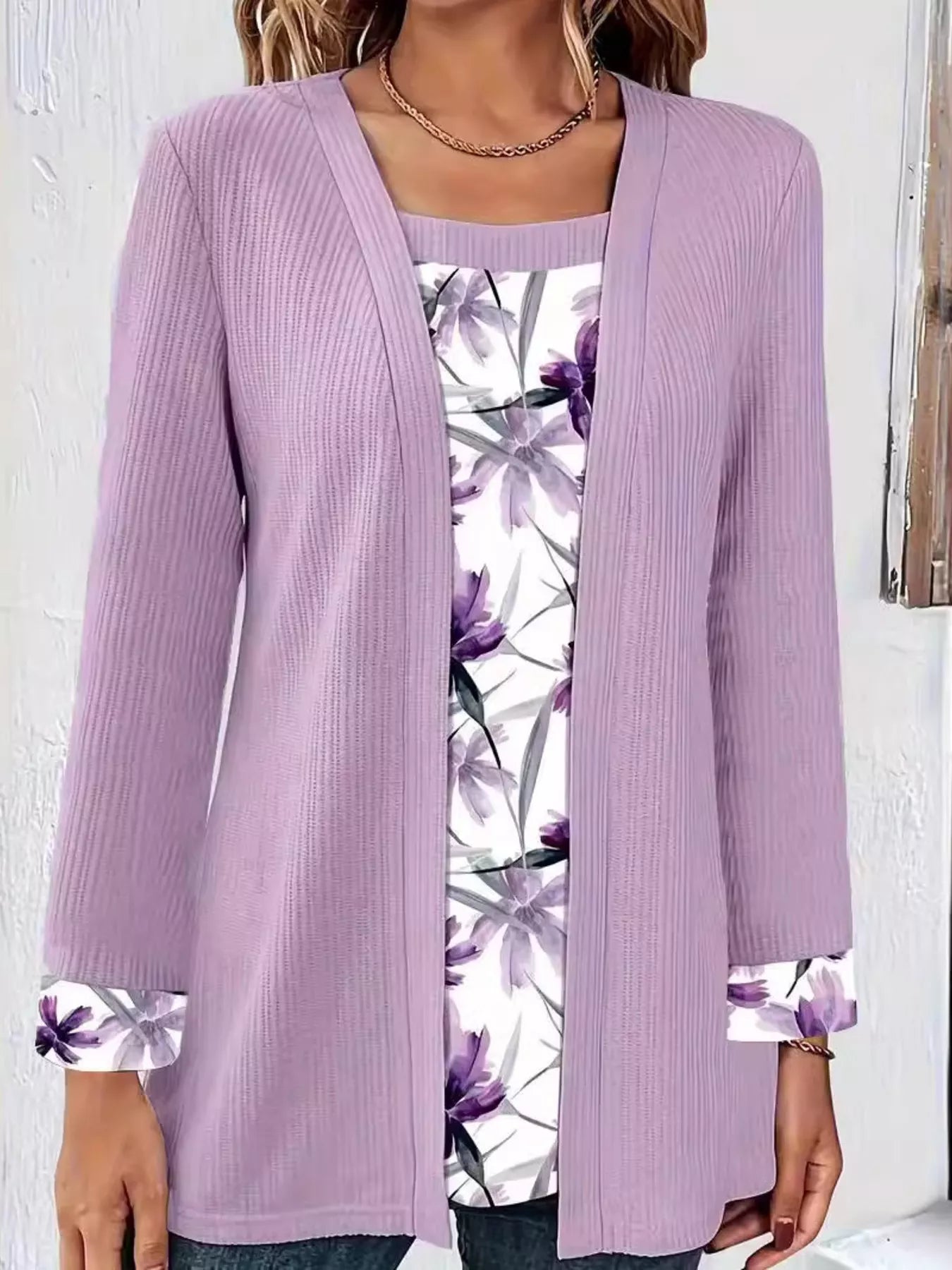 Woman wearing a faux two-piece top with a ribbed outer layer and floral underlayer at the neckline and sleeve cuffs.