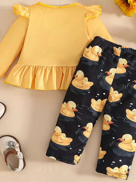 Two-piece baby outfit featuring a yellow long-sleeve ruffled top with a cute duck print and black pants with yellow duck patterns, displayed with floral sandals.