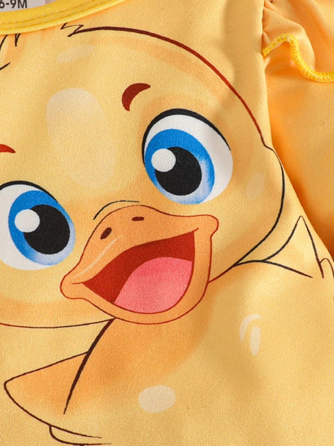 Two-piece baby outfit featuring a yellow long-sleeve ruffled top with a cute duck print and black pants with yellow duck patterns, displayed with floral sandals.