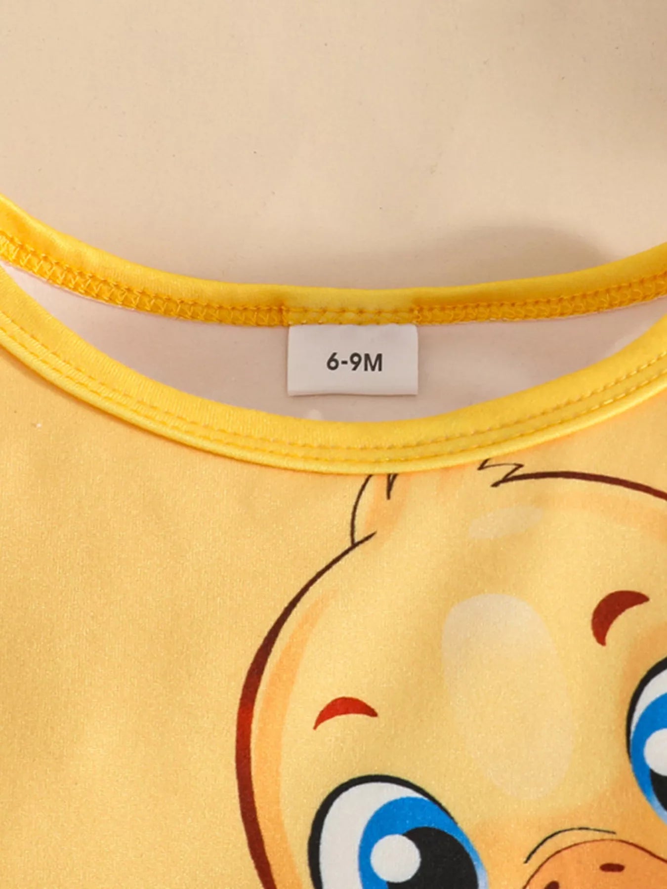 Two-piece baby outfit featuring a yellow long-sleeve ruffled top with a cute duck print and black pants with yellow duck patterns, displayed with floral sandals.