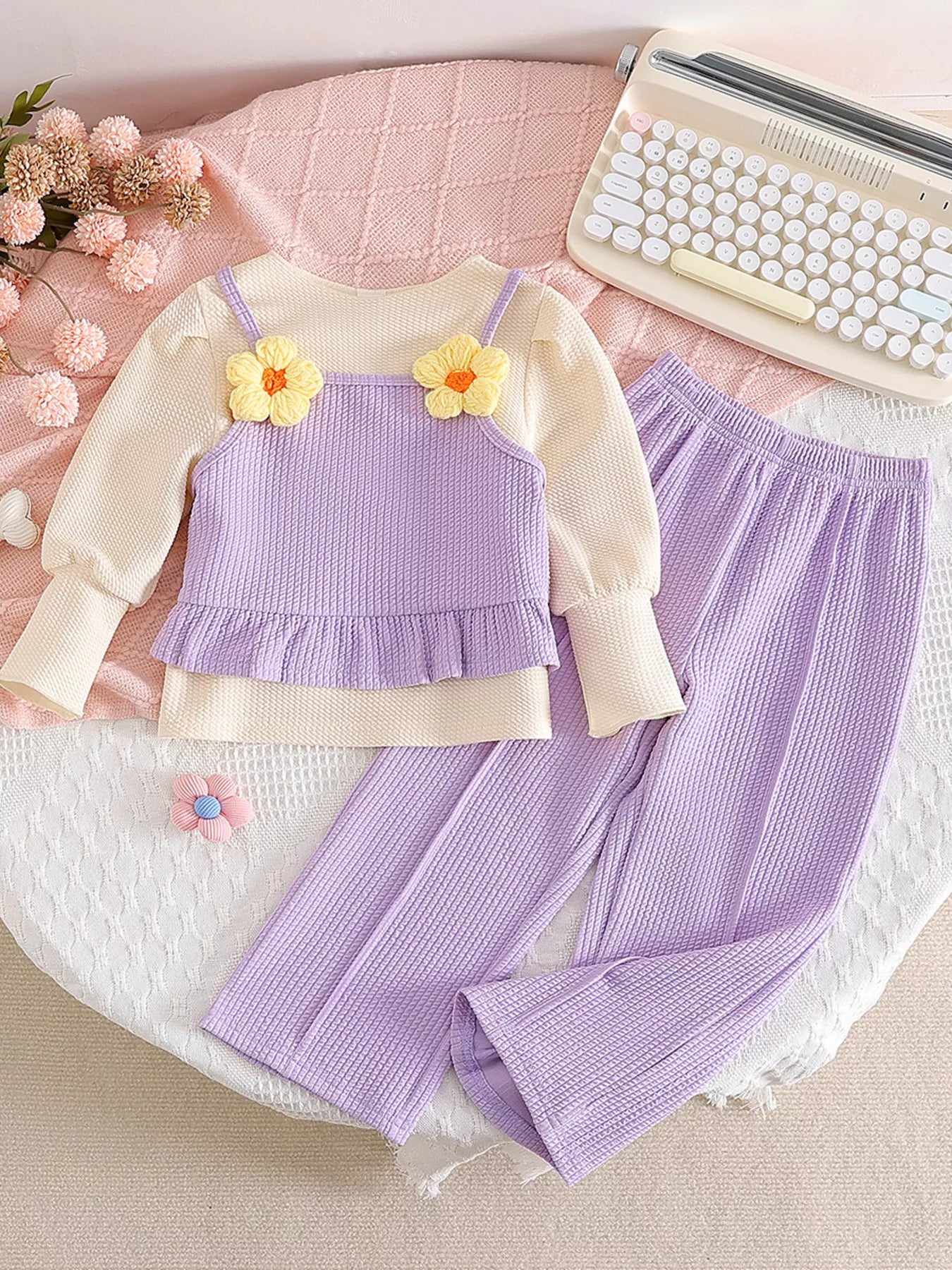 Children’s two-piece outfit with lavender ribbed pants, matching frill top, daisy appliqué details, and soft cotton-blend fabric.
