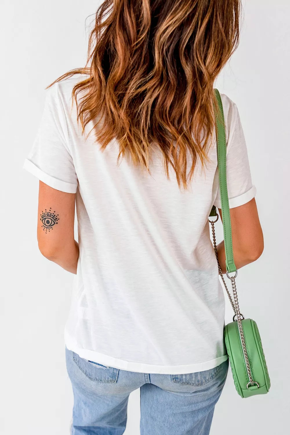 White short sleeve graphic tee with three green fish illustrations on the front, styled with denim jeans and a green bag.
