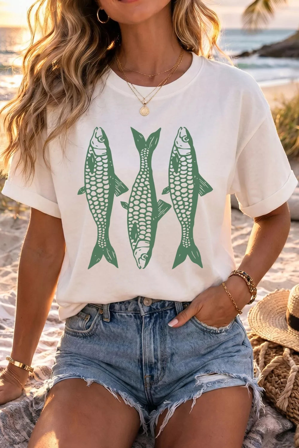 White short sleeve graphic tee with three green fish illustrations on the front, styled with denim jeans and a green bag.